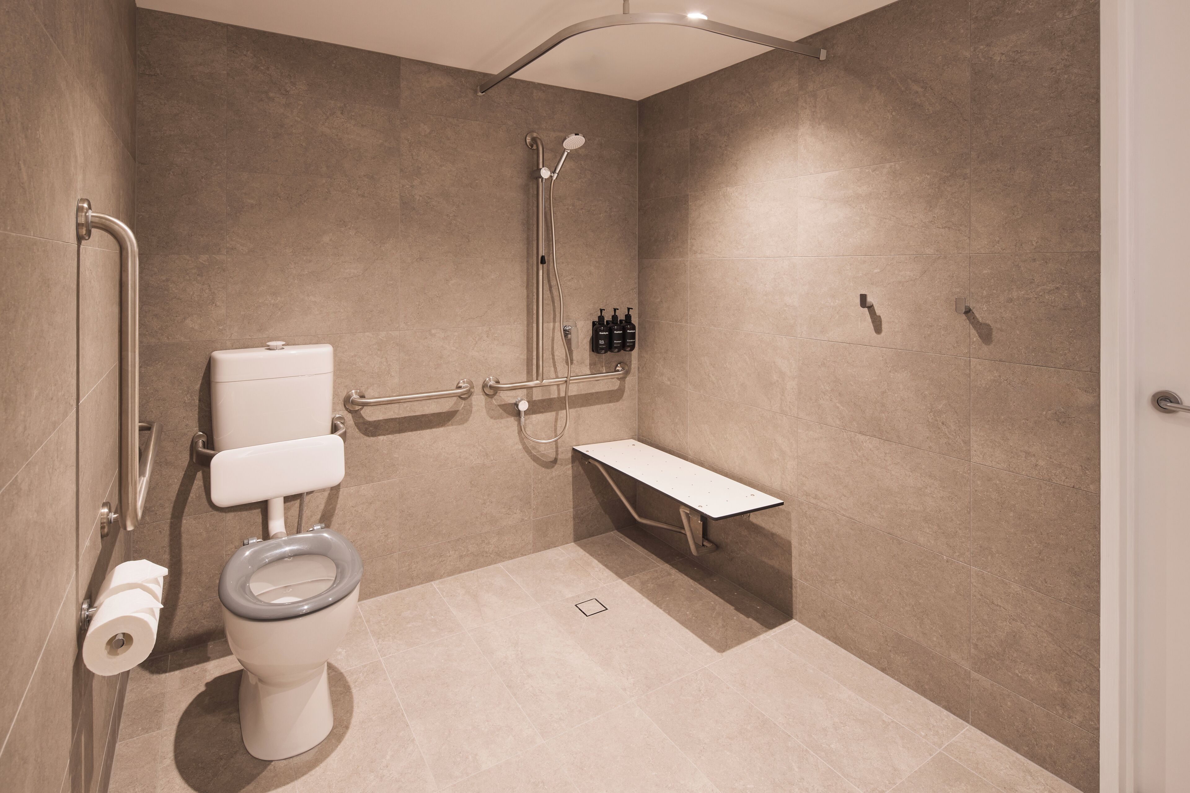 Un baño moderno con inodoro, ducha y barras de apoyo.