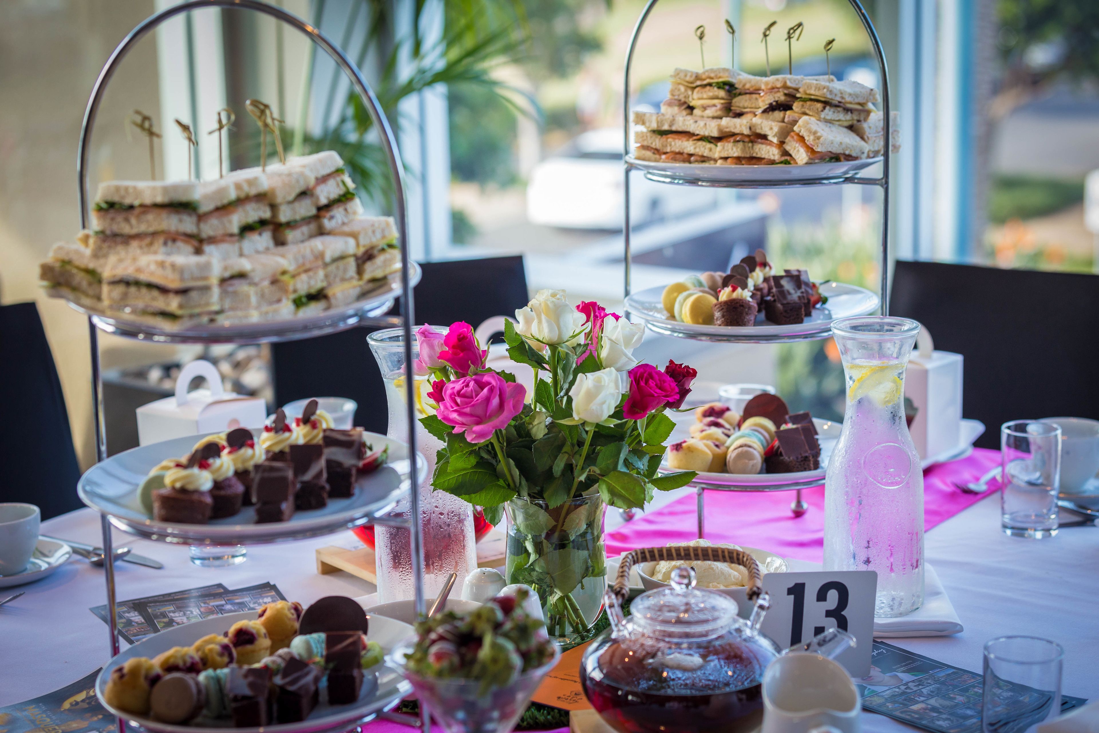 A buffet table with various desserts, sandwiches, and a vase of flowers.