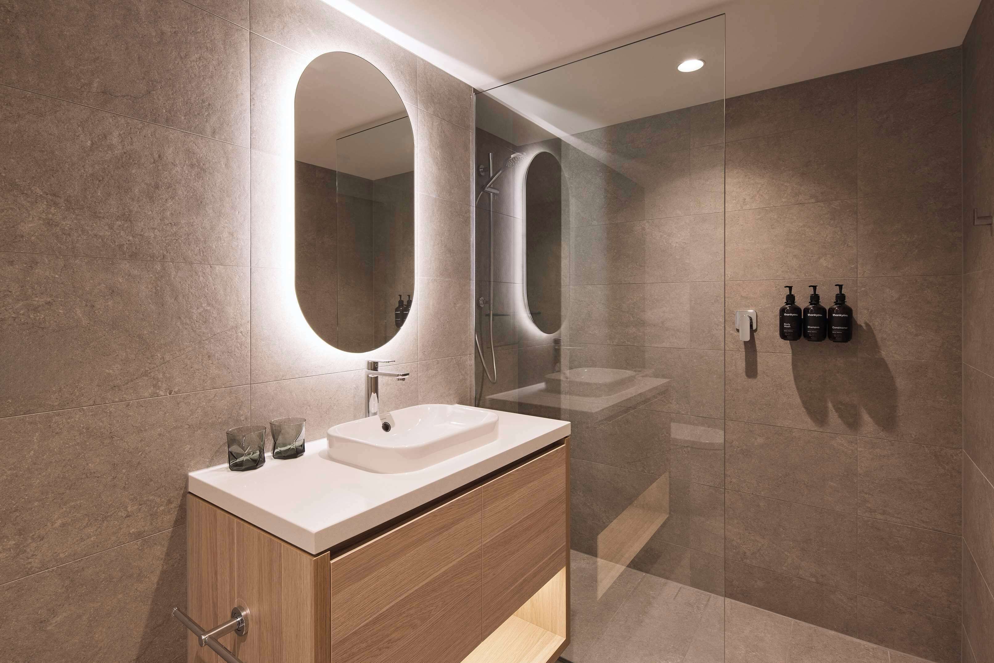 A modern bathroom with a large mirror, a sink, and a shower area.