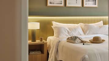 A neatly made bed with white linens, a lamp, and a hat on the side.