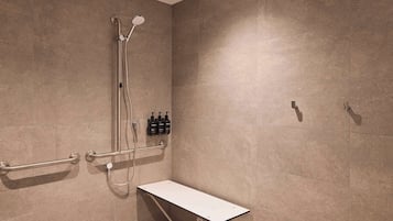 Ein Duschbereich mit Sitzbank, Haltegriffen und einer Handbrause.