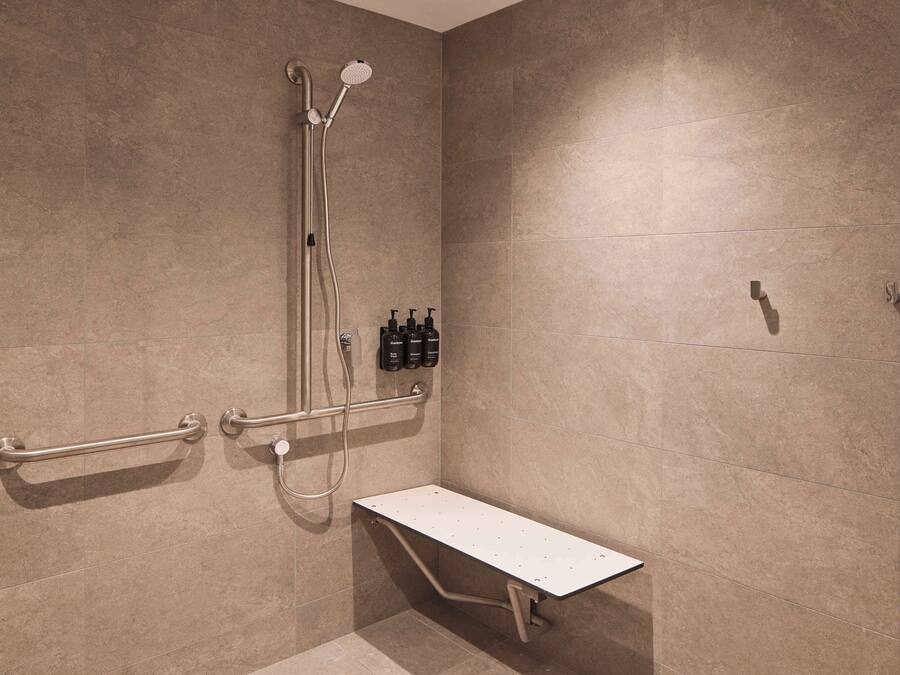 Ein Duschbereich mit Sitzbank, Haltegriffen und einer Handbrause.