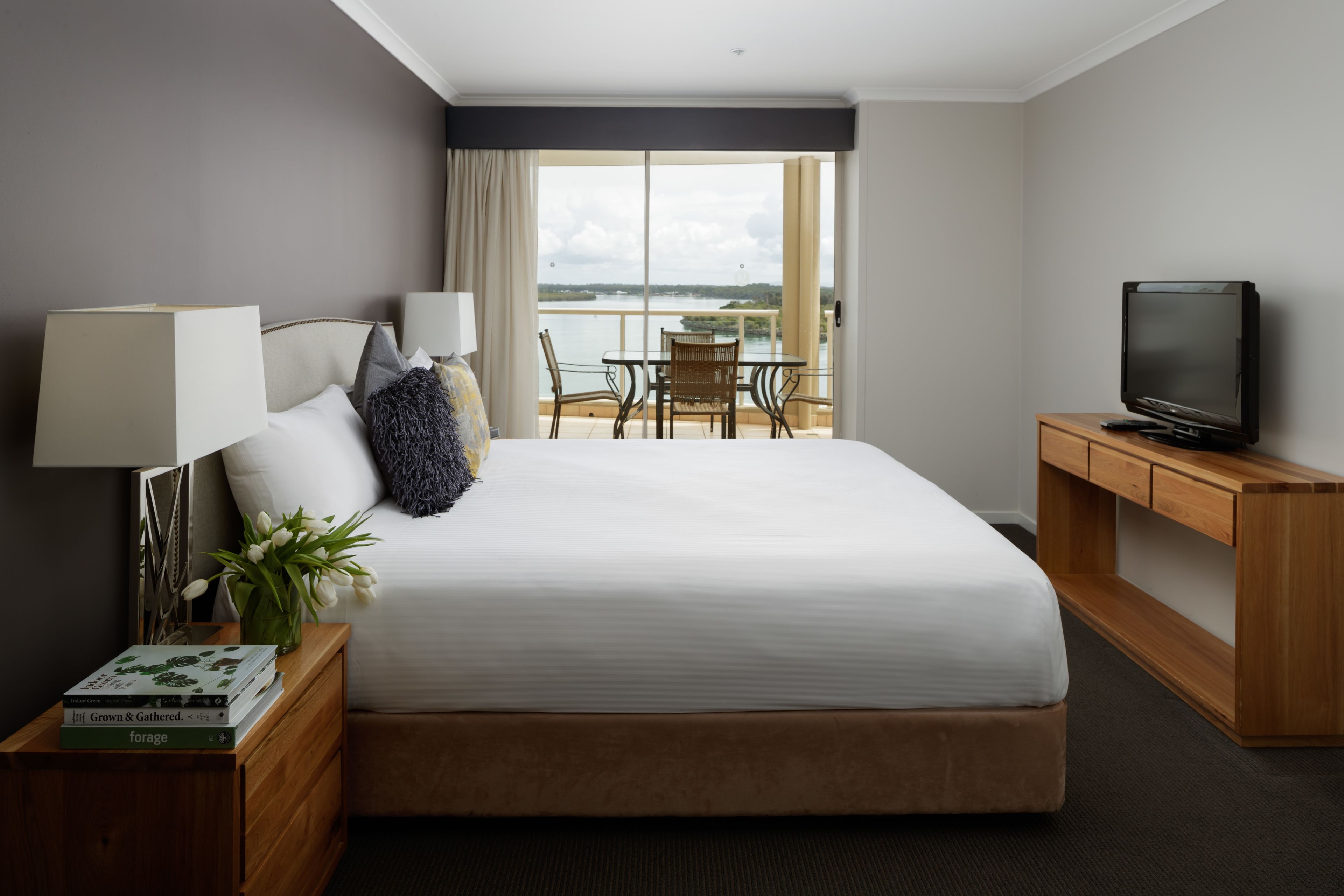 Habitación de hotel con una cama grande, televisión, escritorio, silla y balcón con vistas al agua.