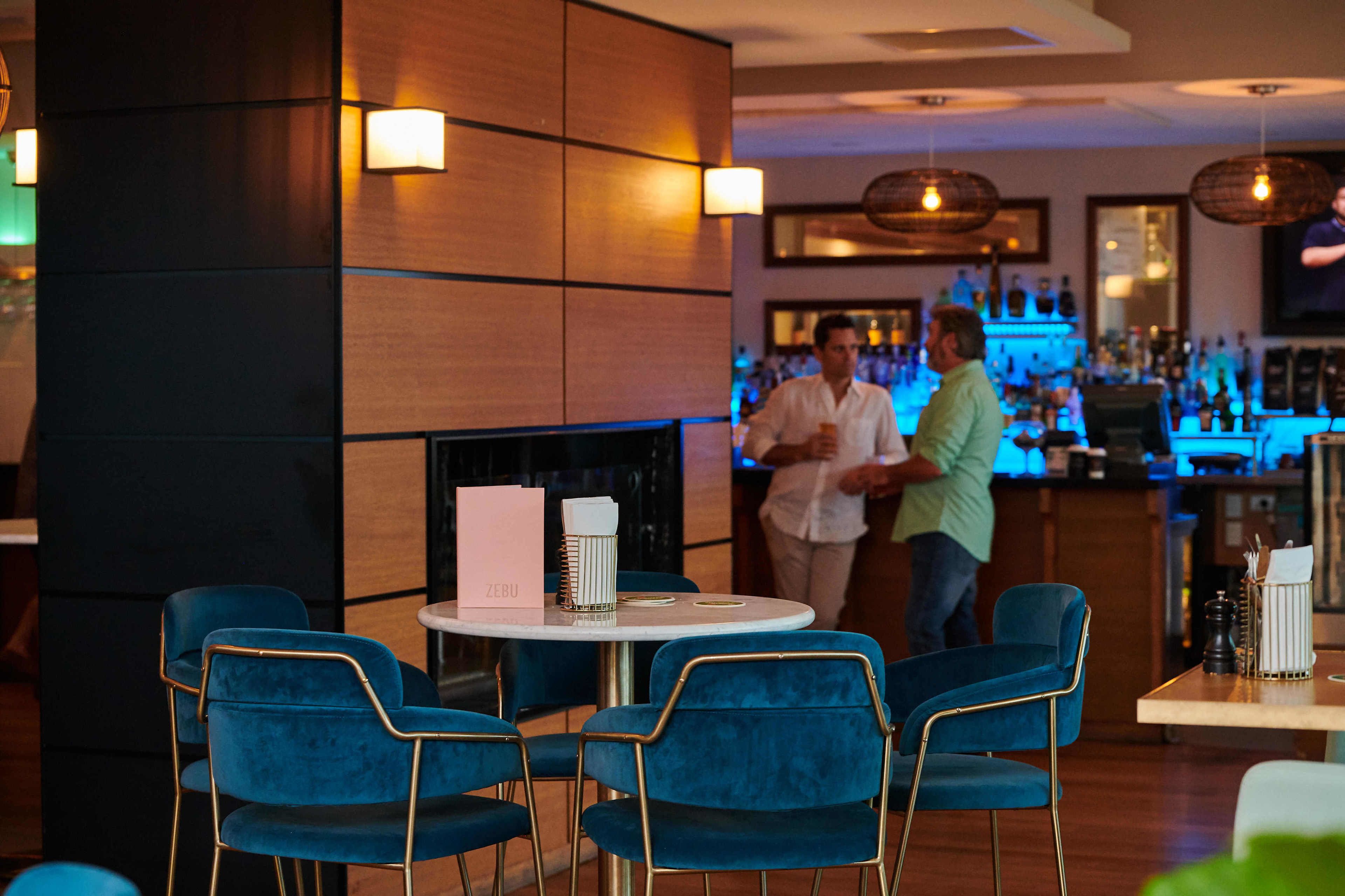Een bar met blauwe stoelen, een witte tafel en een open haard.