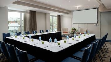A conference room with a long table, chairs, water bottles, apples, and a projector screen.