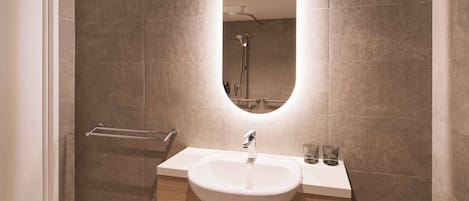 Un baño moderno con un espejo ovalado grande, un lavabo blanco y un perchero para toallas.