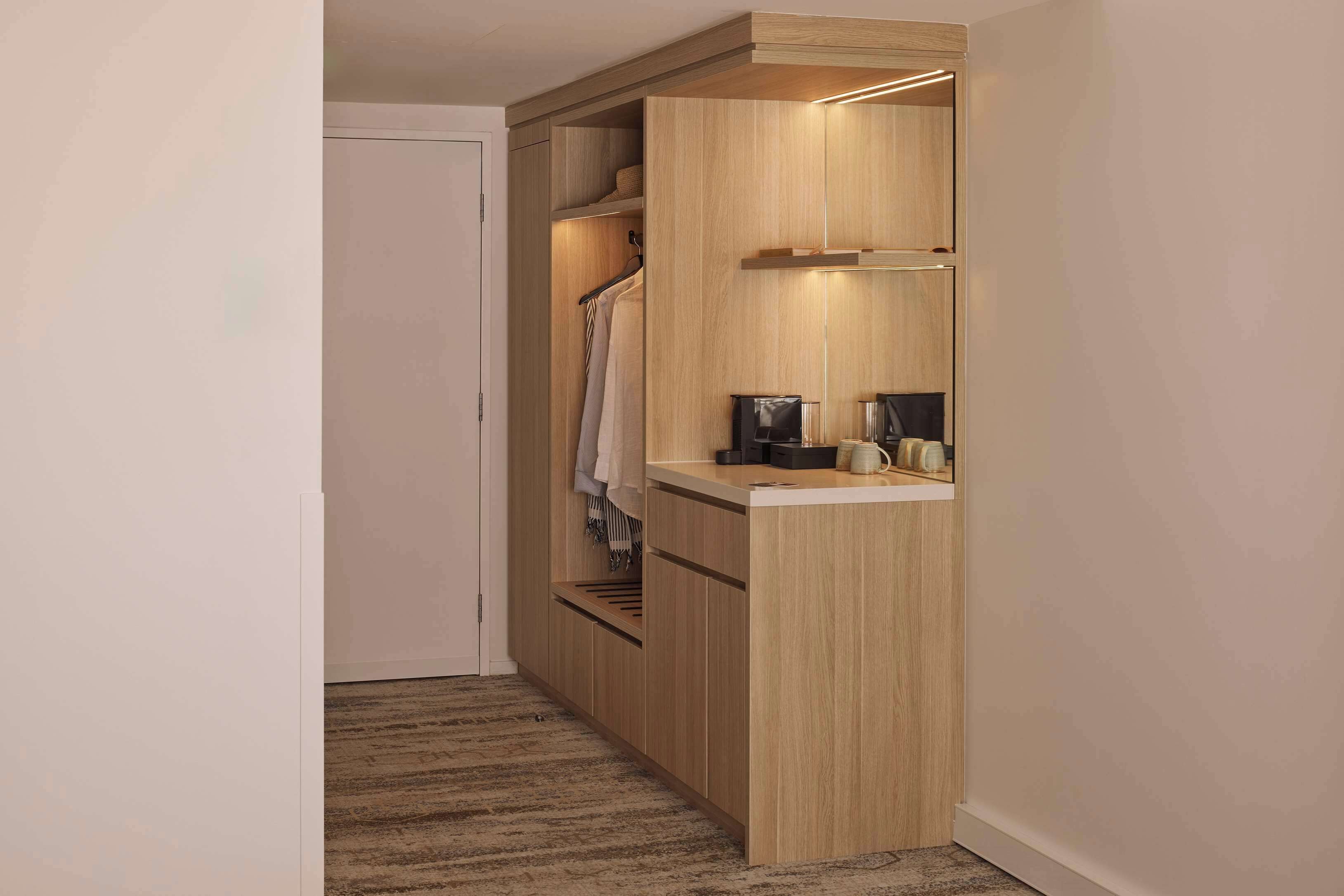 Un couloir étroit avec une armoire en bois, un petit comptoir avec une bouilloire et un manteau accroché.