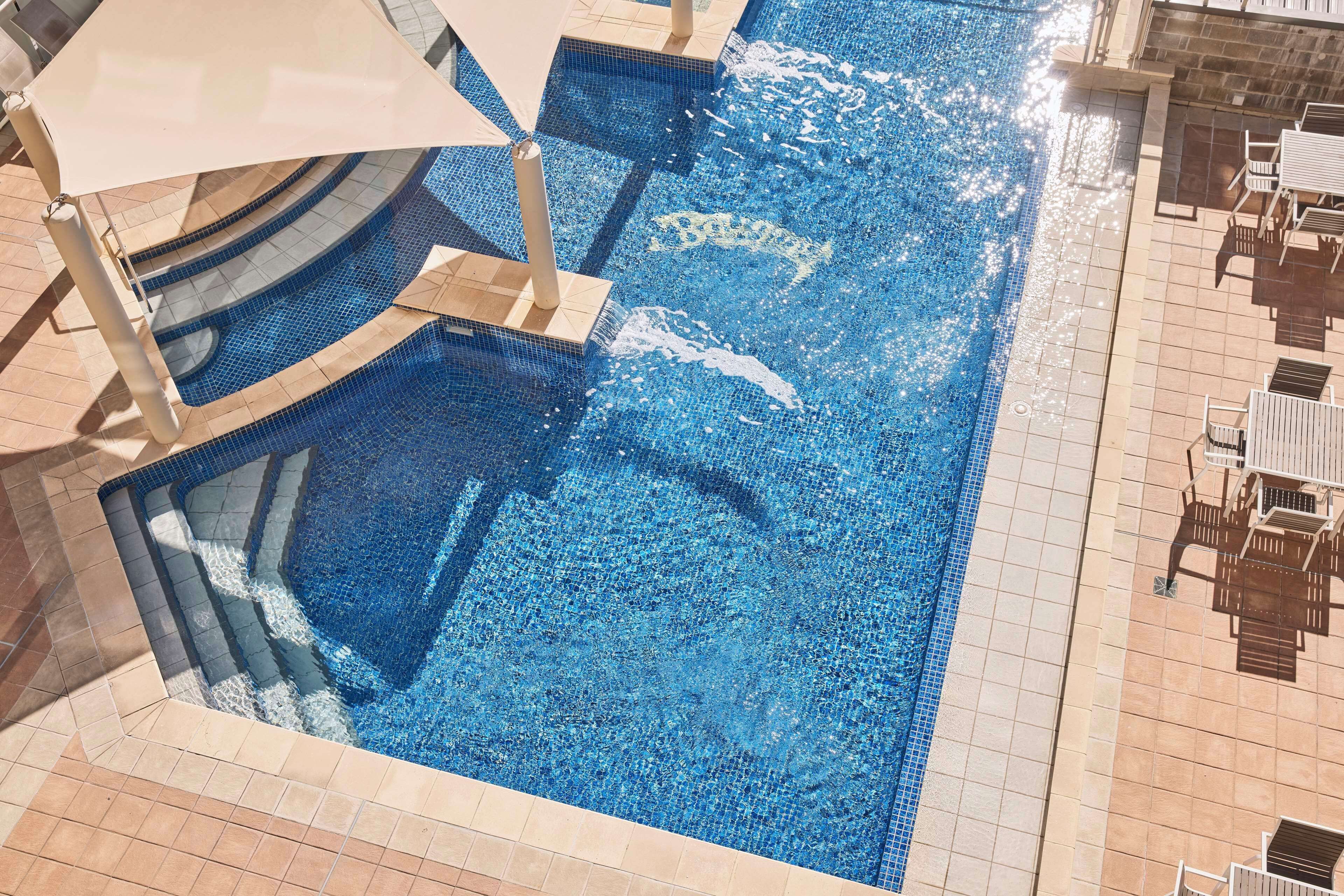 A swimming pool with a tiled edge, sun loungers, and a shaded area.