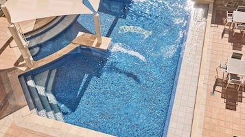 A swimming pool with a tiled edge, sun loungers, and a shaded area.