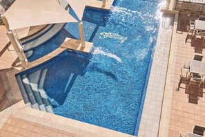 Una piscina con borde de azulejos, tumbonas y una zona con sombra.