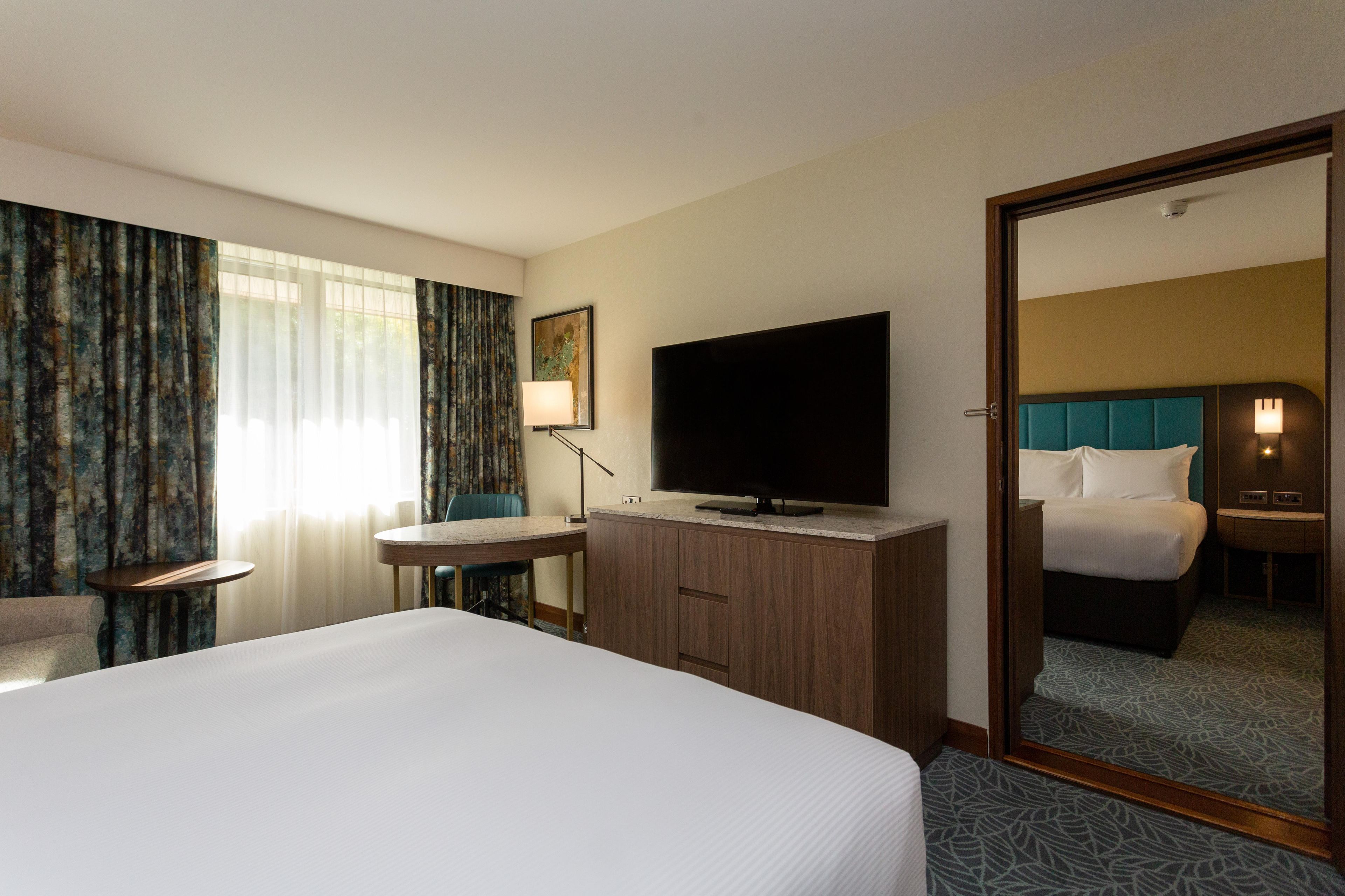 Habitación de hotel con cama, escritorio, televisor y espejo.