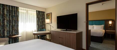 Habitación de hotel con cama, escritorio, televisor y espejo.