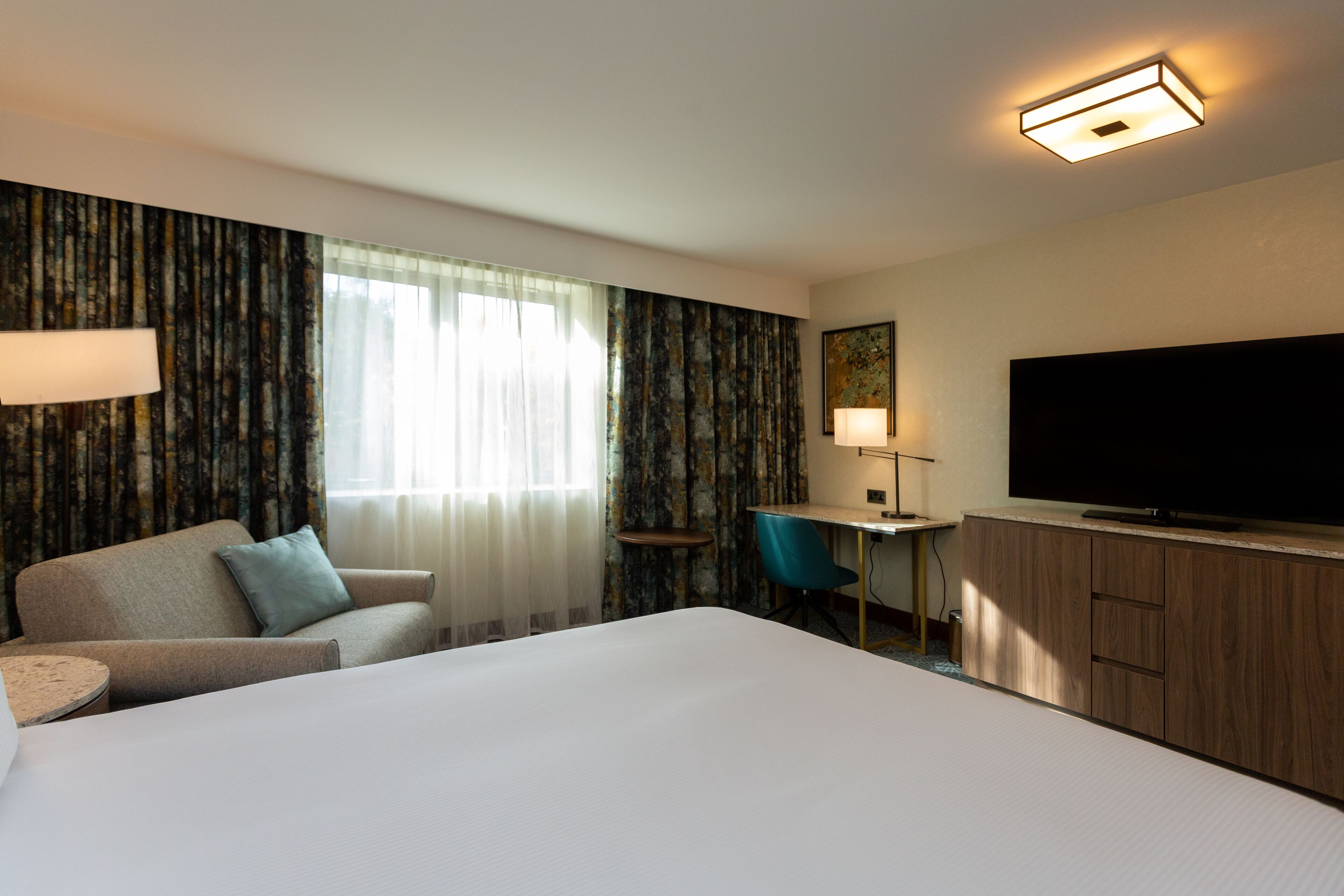 A hotel room with a large bed, a desk with a chair, a television, and curtains.