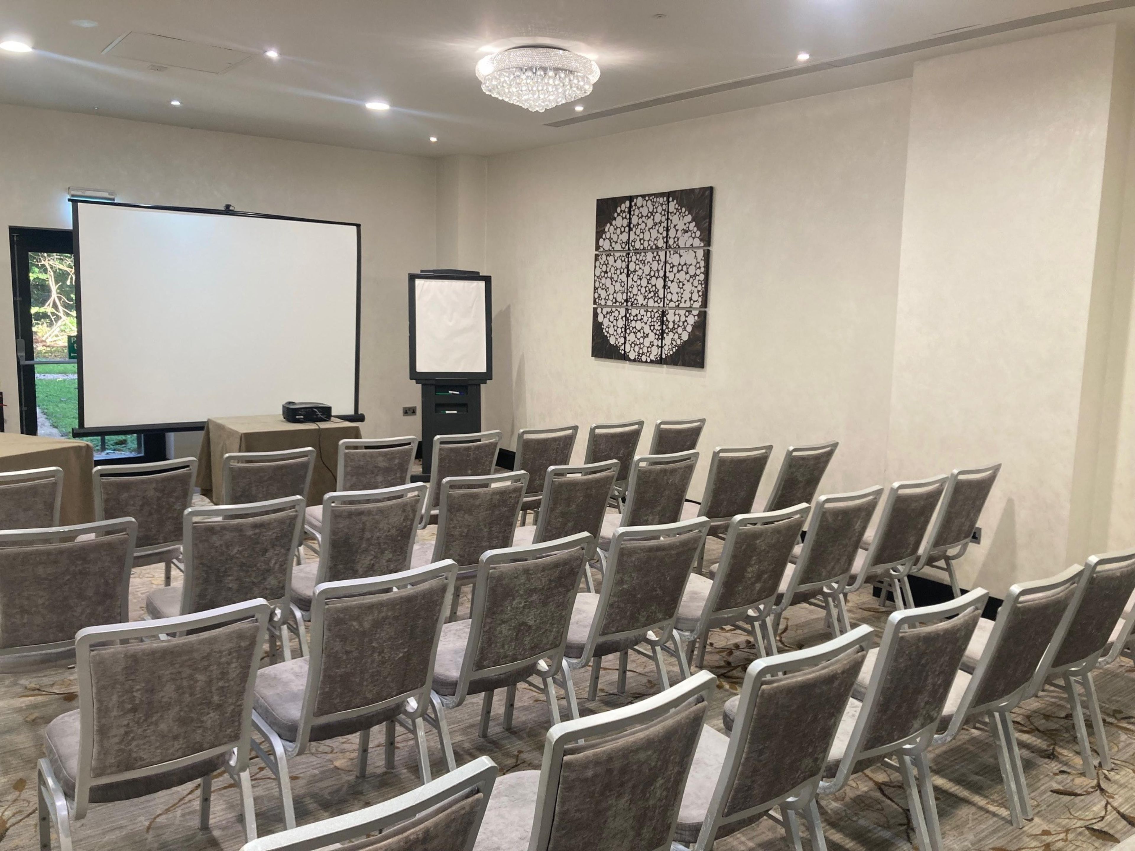 A conference room with rows of chairs, a projector screen, a whiteboard, and a decorative wall piece.