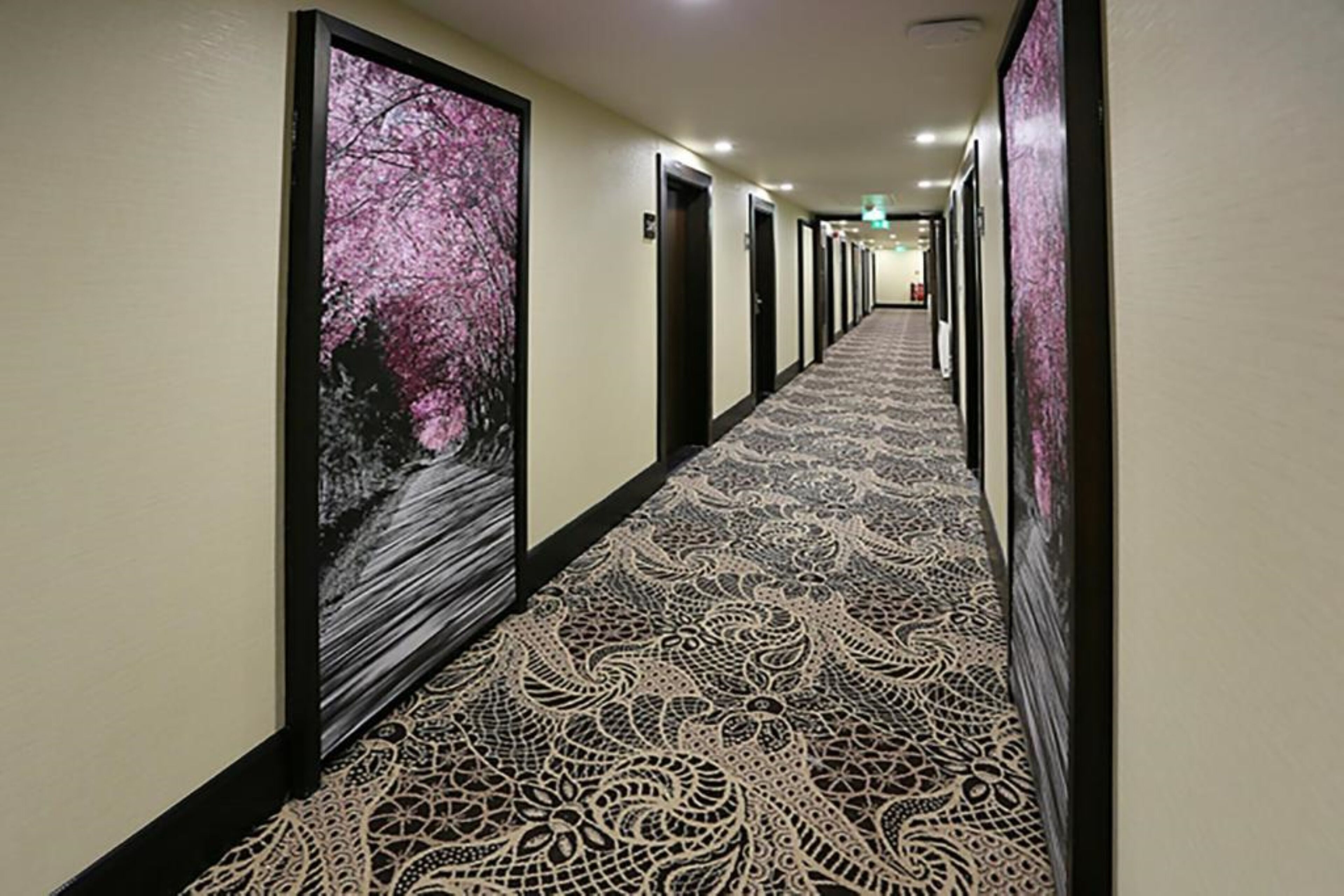 A hotel hallway with patterned carpet and framed artwork on the walls.