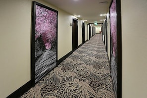 A hotel hallway with patterned carpet and framed artwork on the walls.