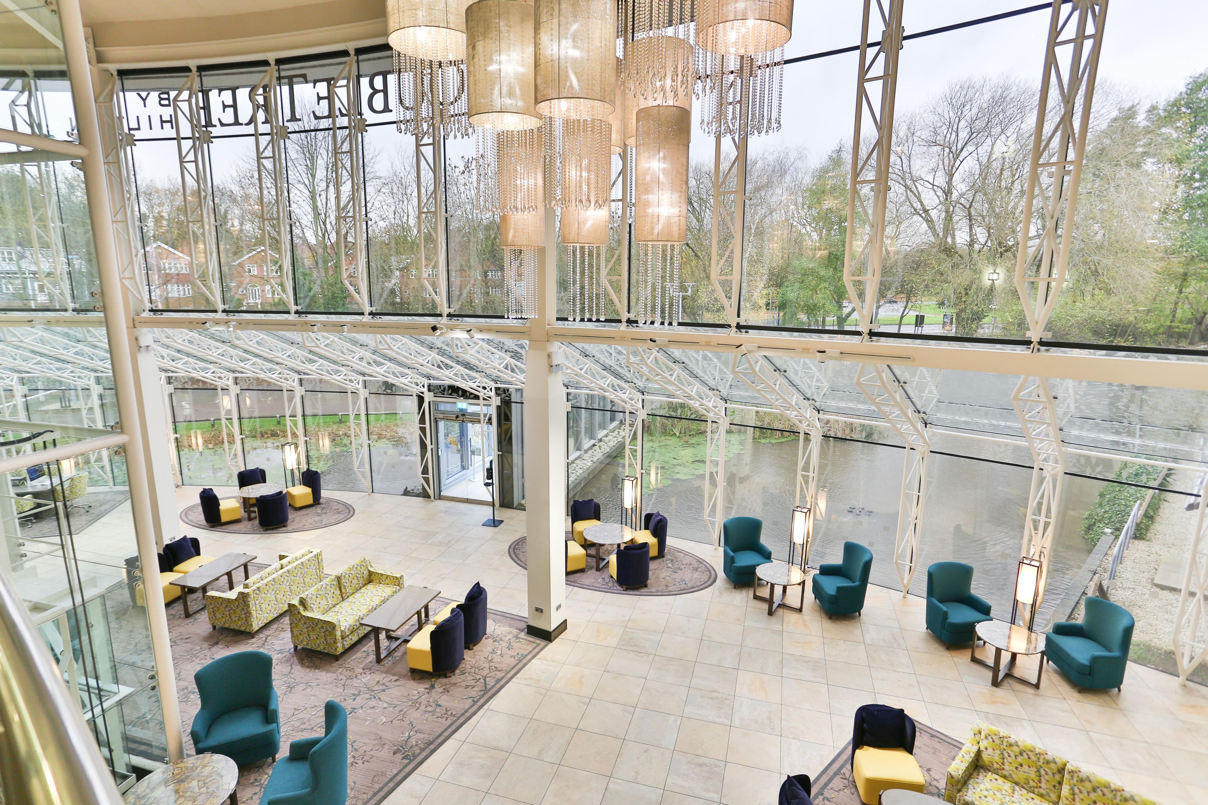 A spacious indoor area with multiple seating arrangements, a glass ceiling, and a view of a water body outside.