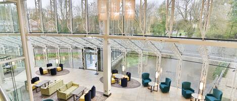 A spacious indoor area with multiple seating arrangements, a glass ceiling, and a view of a water body outside.