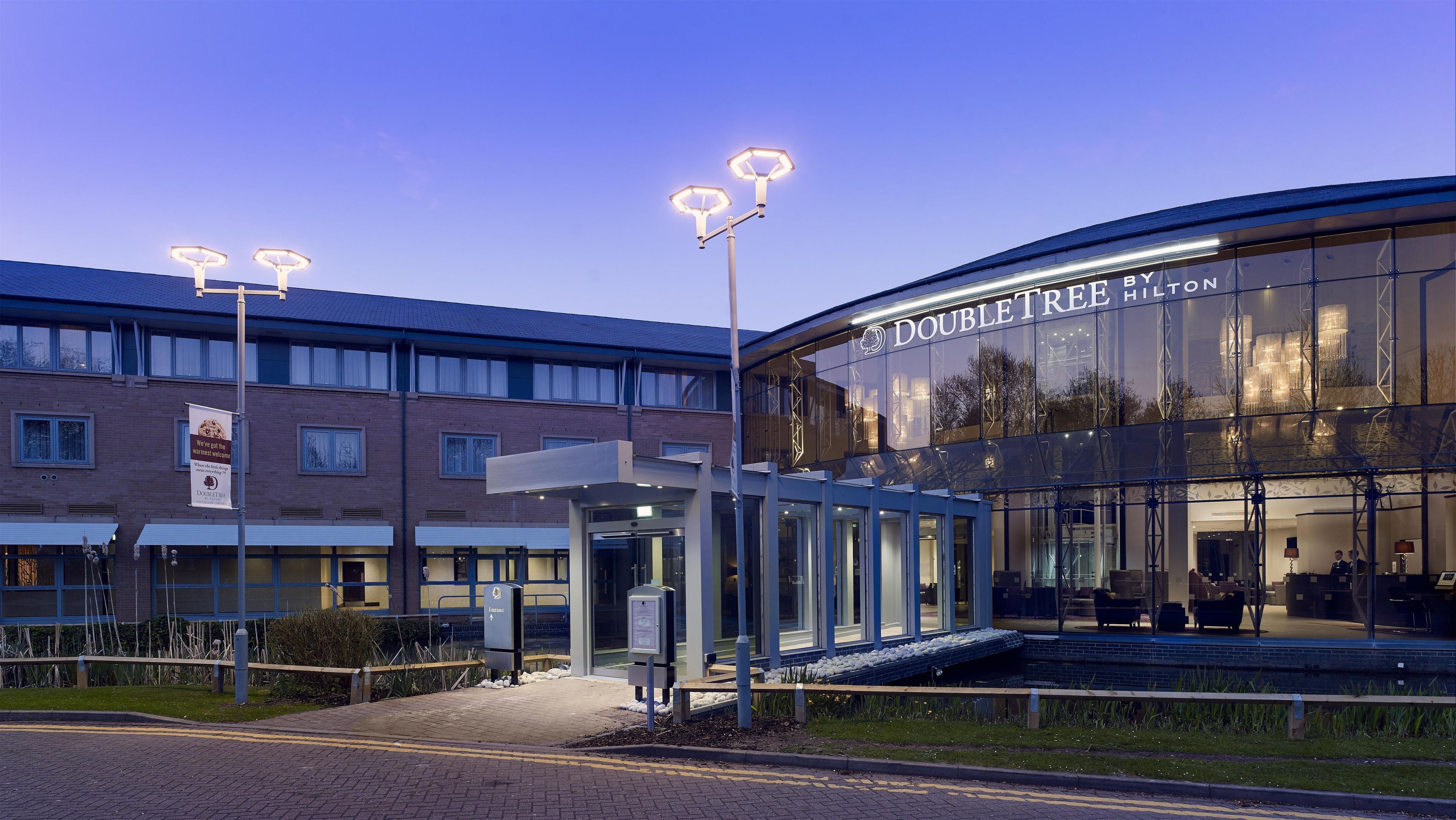 A hotel entrance with a glass facade, a covered waiting area, and a sign reading 'DOUBLETREE HOTEL'.
