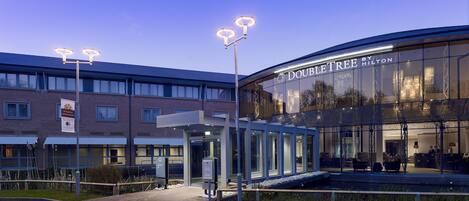 A hotel entrance with a glass facade, a covered waiting area, and a sign reading 'DOUBLETREE HOTEL'.
