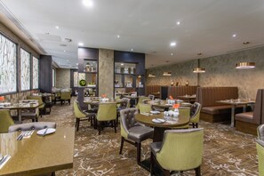 A restaurant with round tables, cushioned booths, and a patterned carpet.
