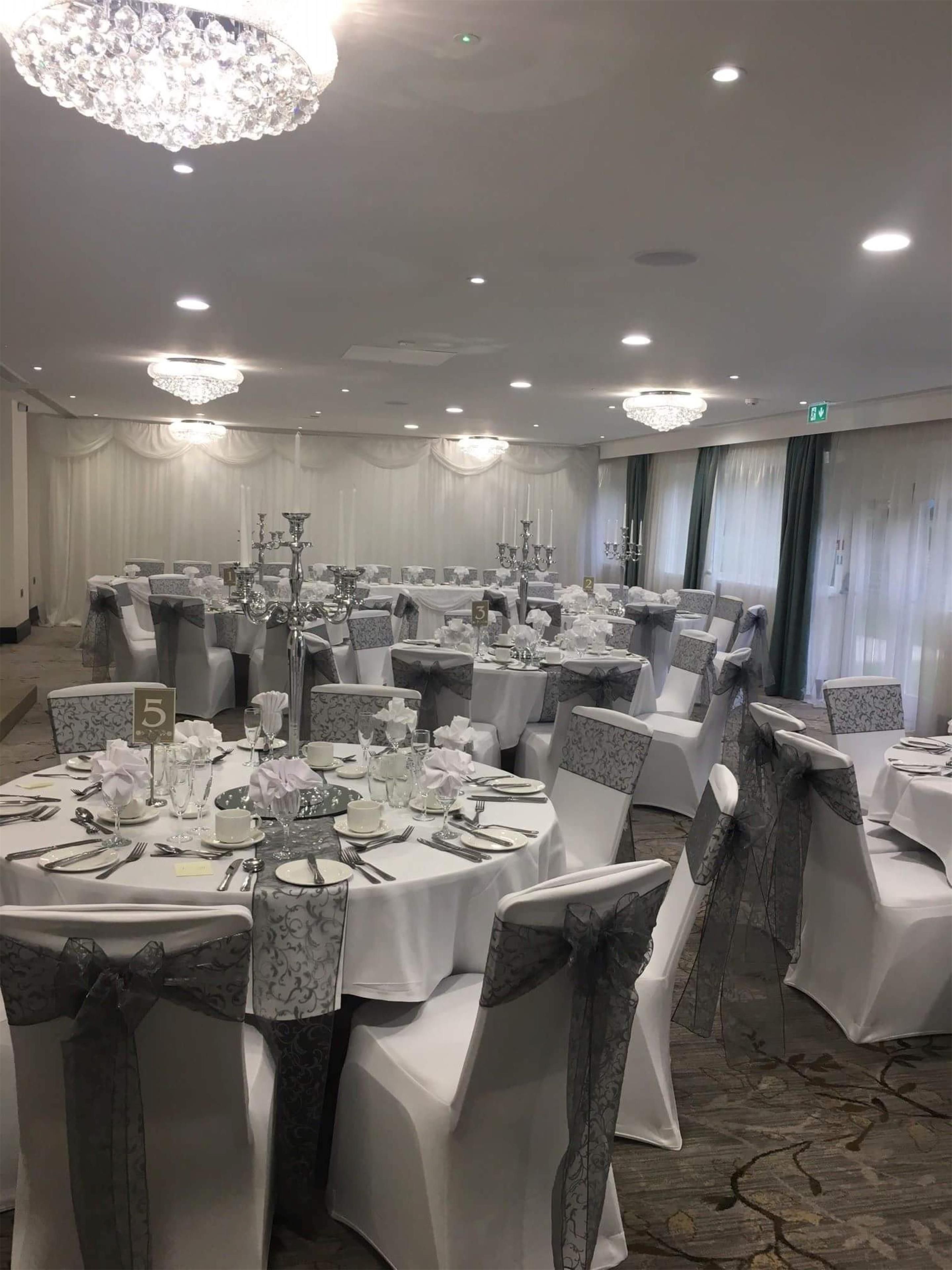 A banquet hall with round tables, white tablecloths, and grey chairs.
