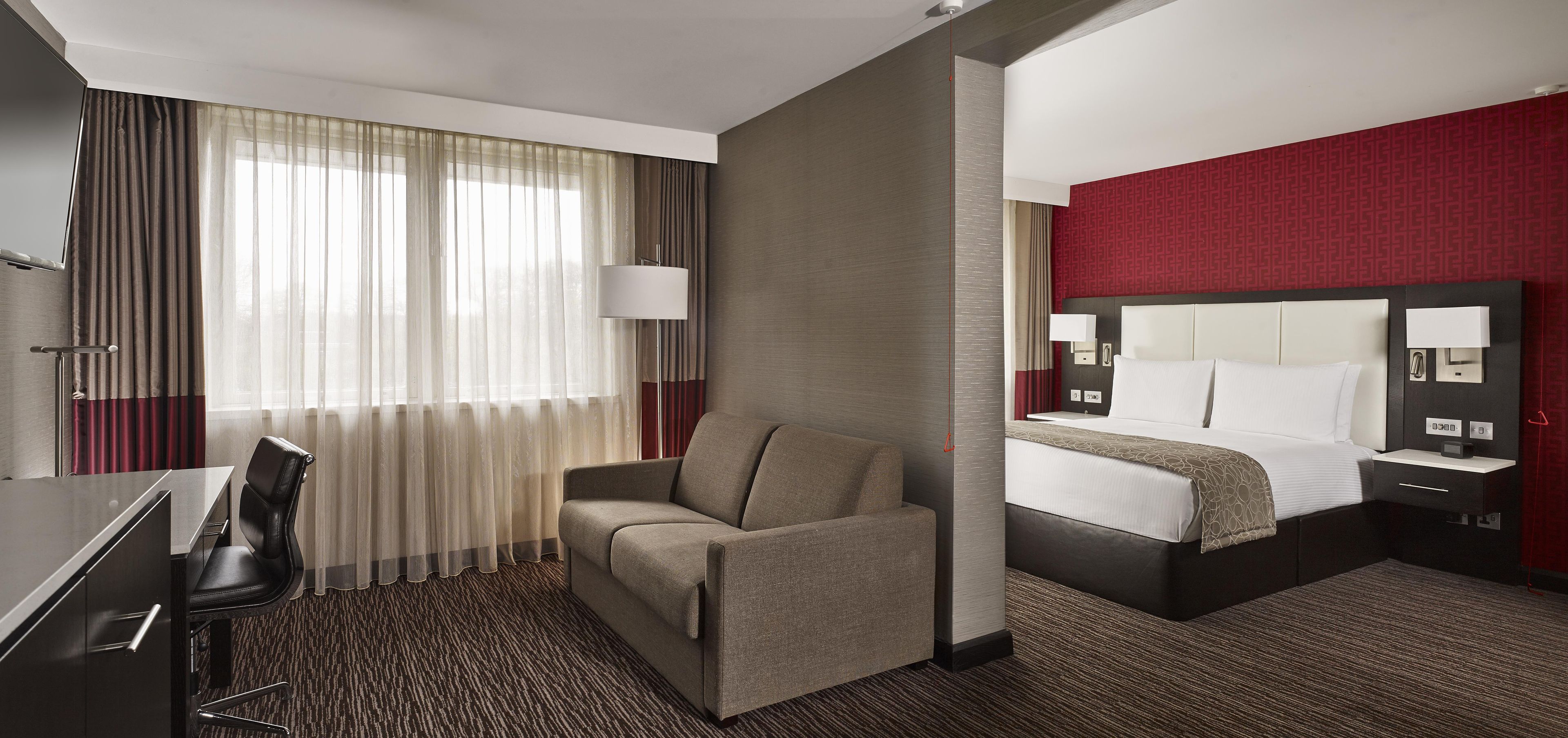 A hotel room with a bed, a desk, a chair, and a large window with curtains.