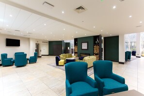 A spacious lobby with teal armchairs, a sofa set, and a fireplace.