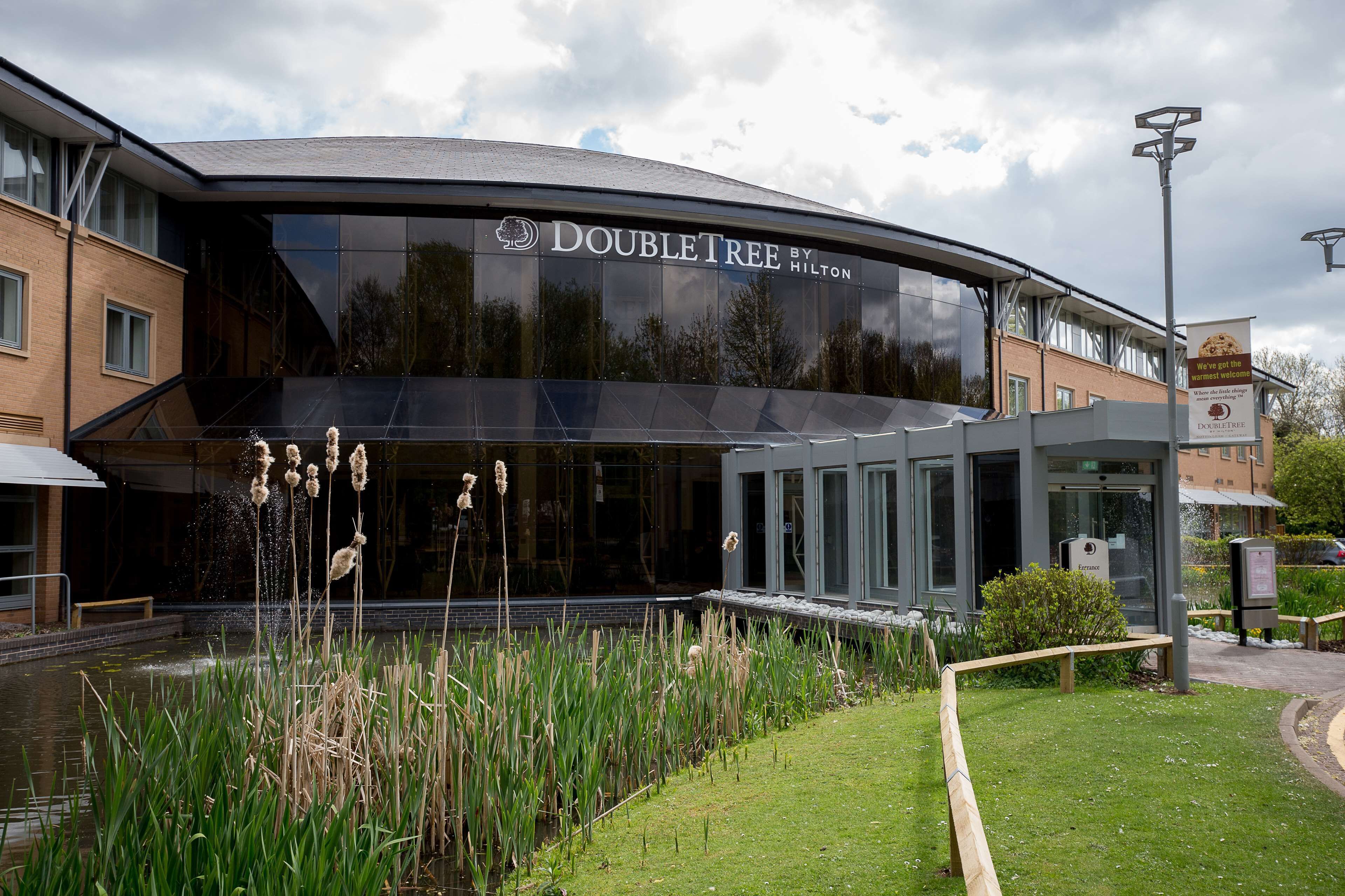 Een DoubleTree by Hilton hotel met een moderne glazen gevel, een aangelegde tuin met waterpartijen, en een heldere lucht.
