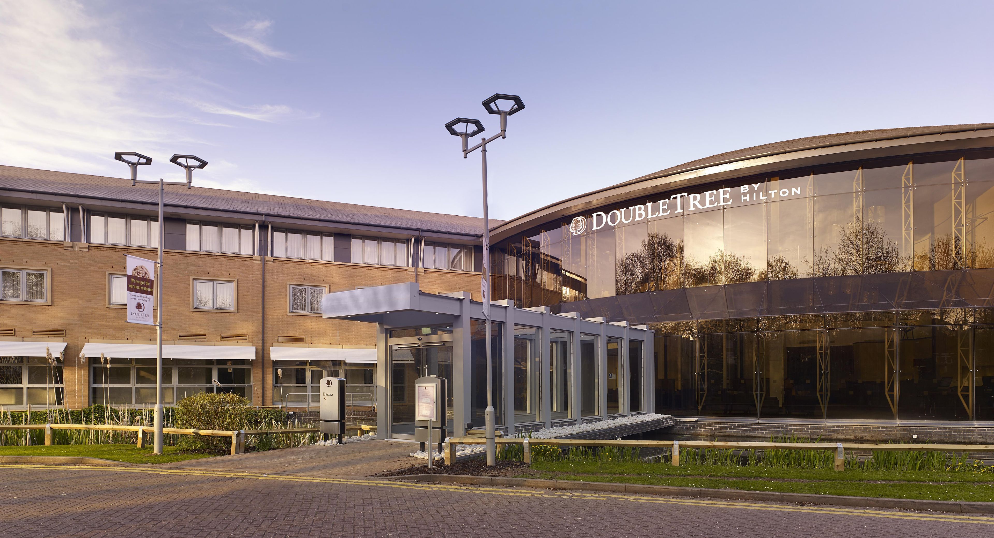 A modern building with a glass facade, a sign reading 'DOUBLETREE by Hilton,' and a covered entrance area.