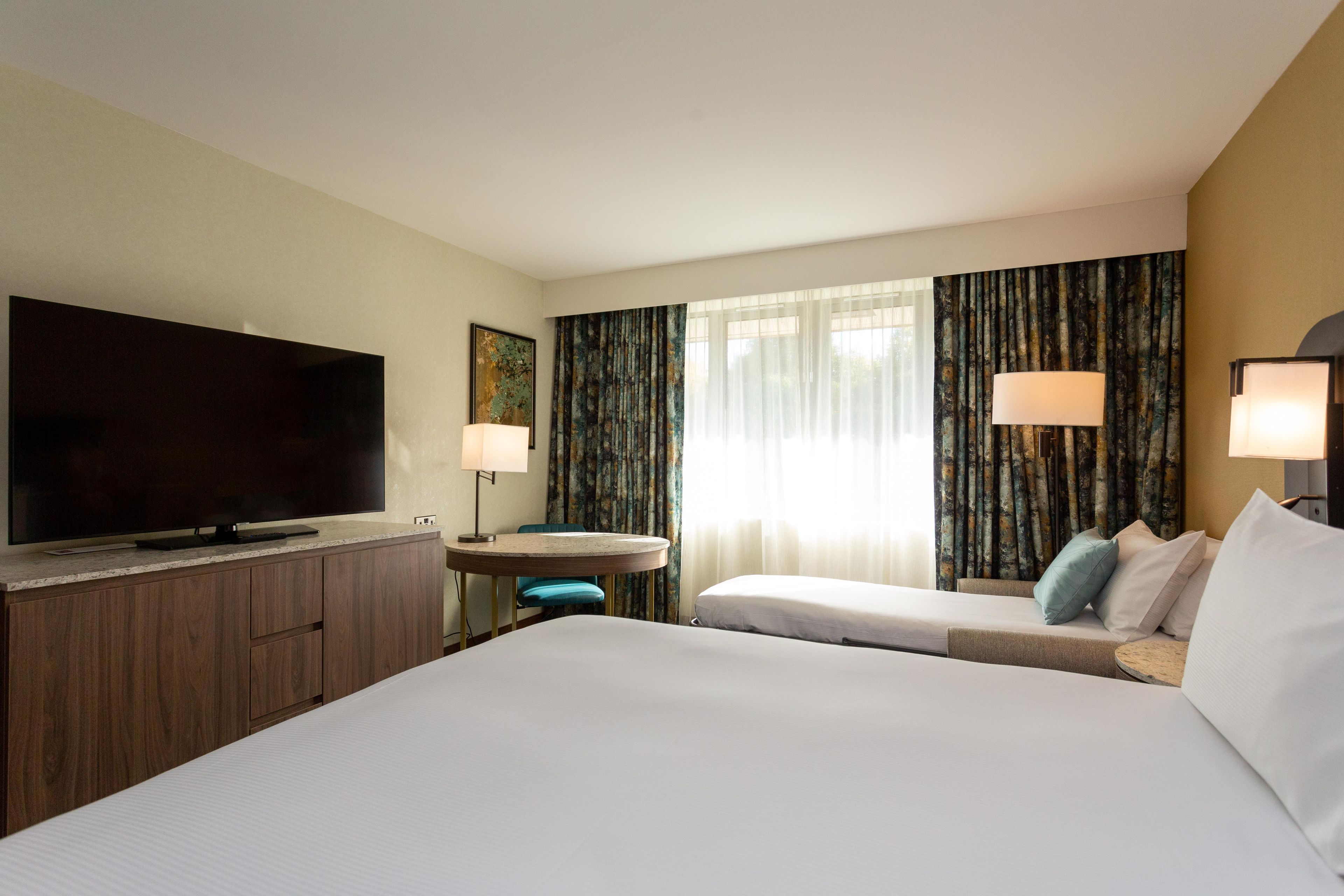 Ein Hotelzimmer mit einem großen Bett, einem Fernseher, einem Schreibtisch mit Stuhl und zwei Lampen.