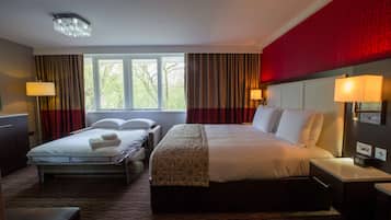 A hotel room with a large bed, a smaller bed, a desk, and a chair. There are two windows with curtains, a chandelier, and a red accent wall.