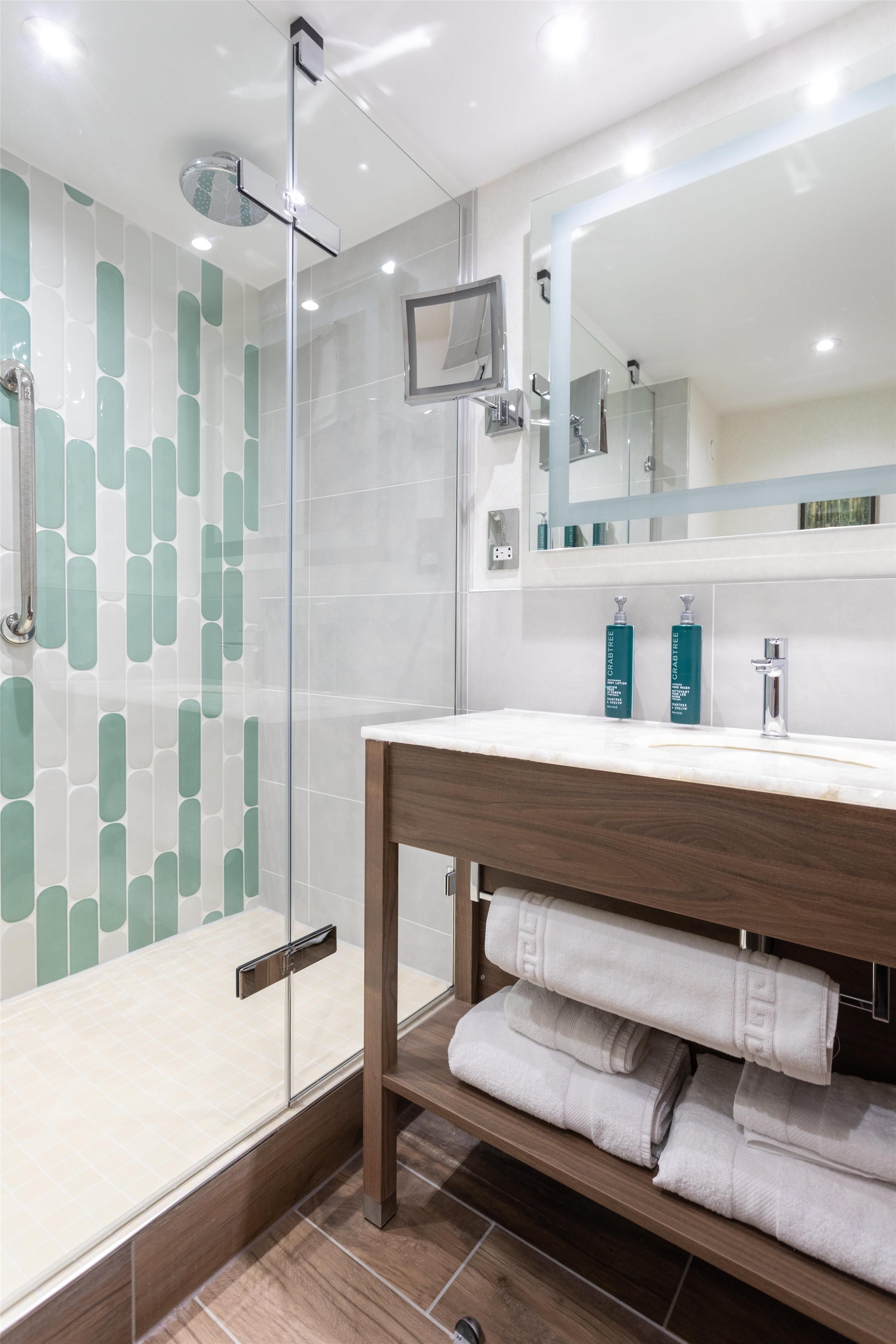A modern bathroom with a glass shower enclosure, a wooden vanity with a mirror, and neatly folded towels.