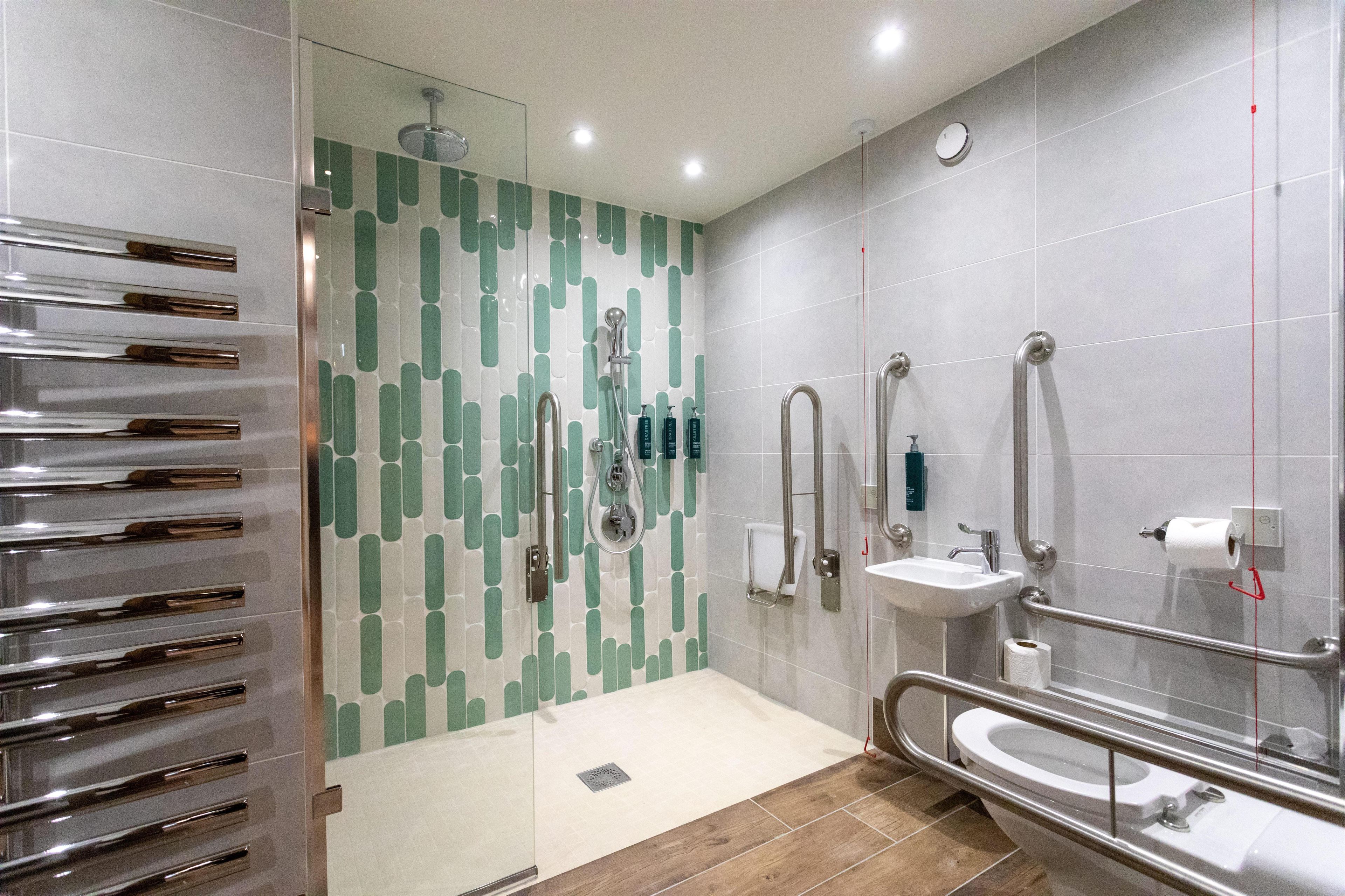 Un baño moderno con cabina de ducha de vidrio, un lavamanos con barra de apoyo y un inodoro con barandilla.