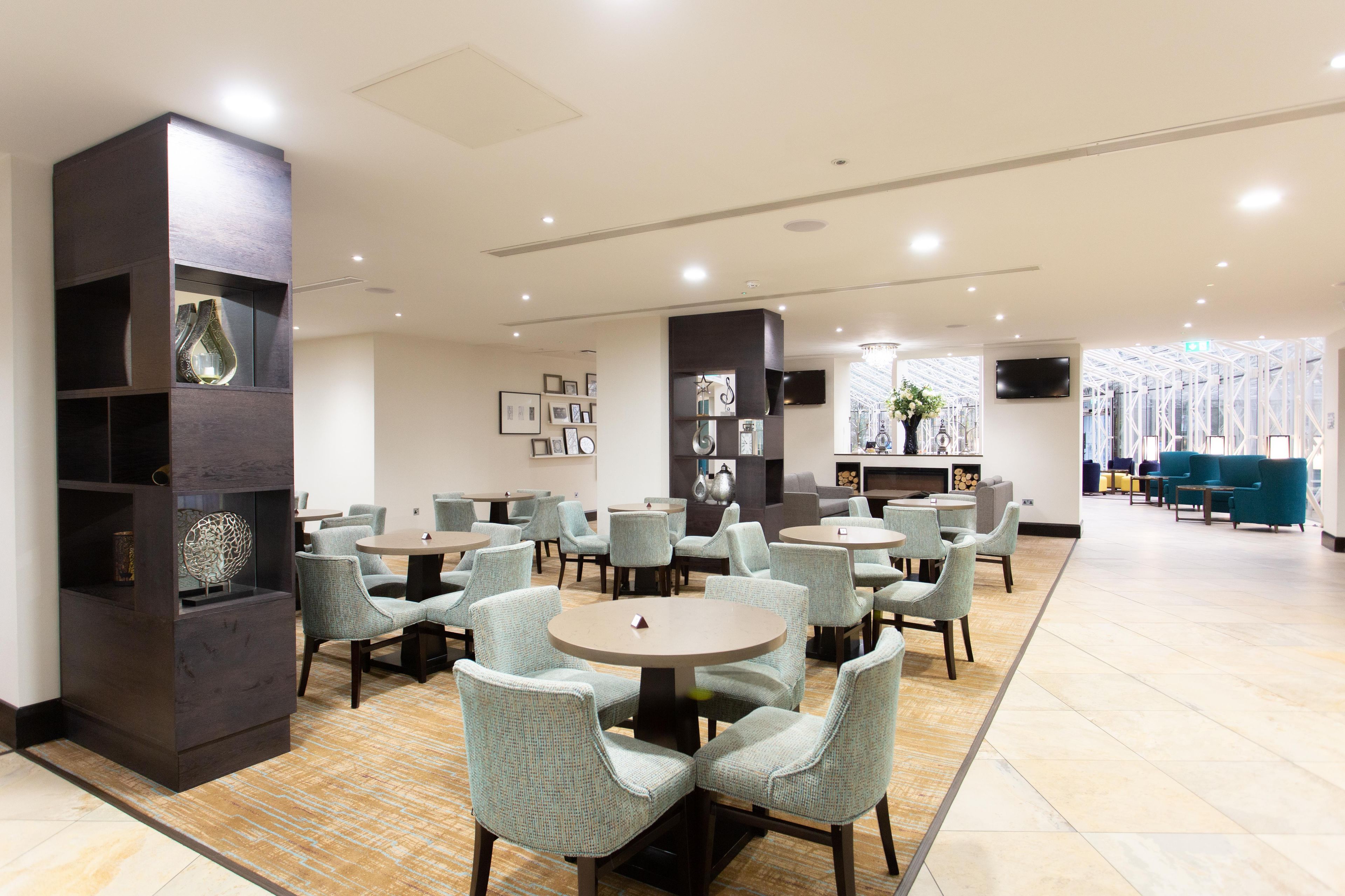 Un hall d’hôtel moderne avec des tables et des chaises rondes, une cheminée et un téléviseur.