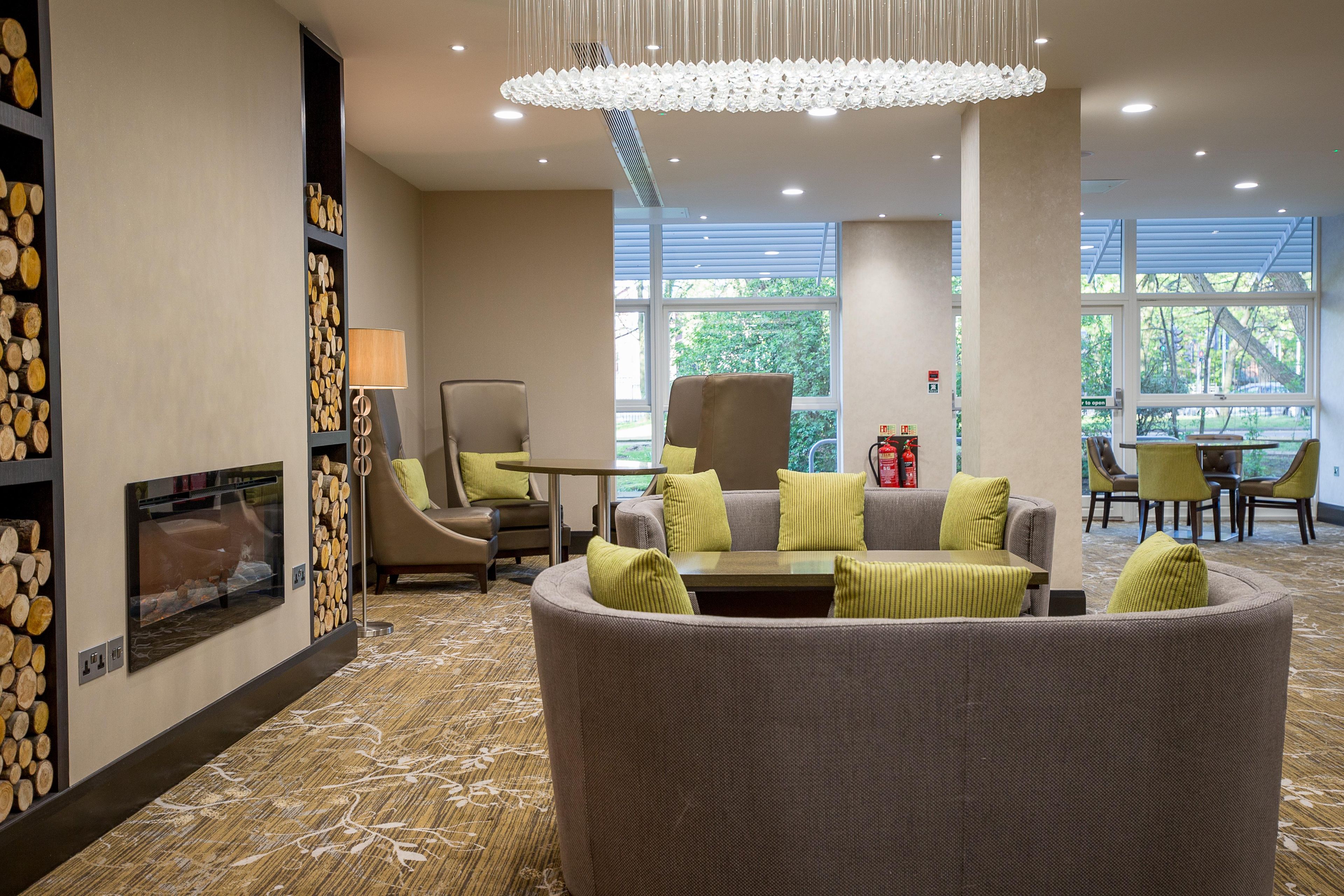 A modern hotel lobby with a fireplace, seating area, and large windows.