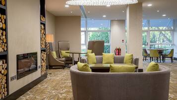 A modern hotel lobby with a fireplace, seating area, and large windows.