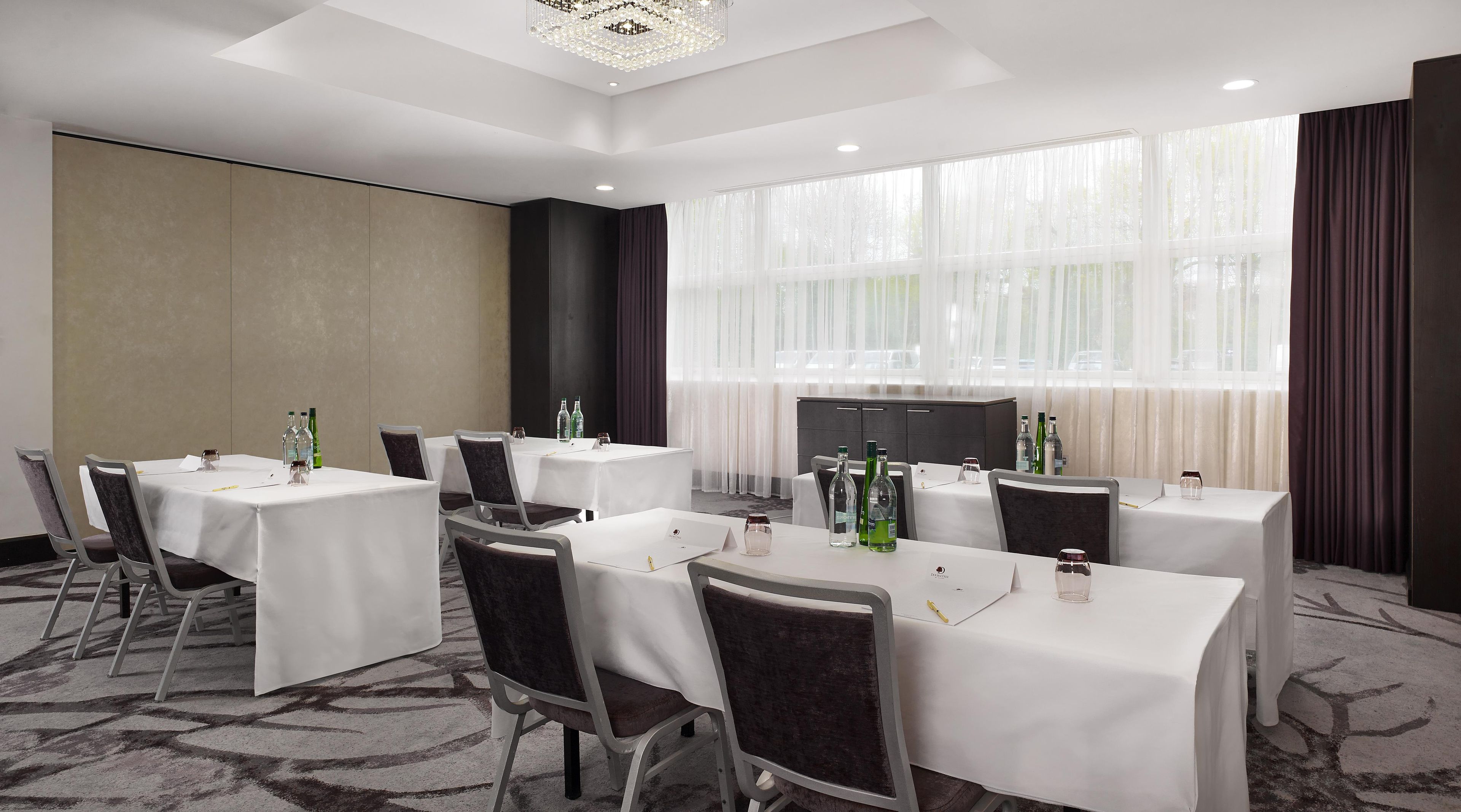 A conference room with tables, chairs, and a large window with curtains.