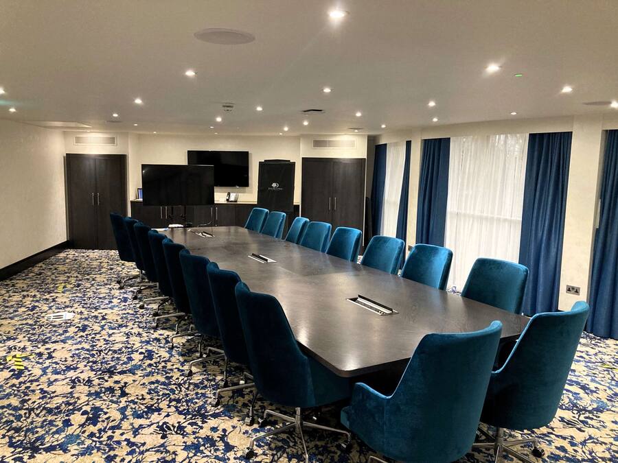 Uma sala de conferências com uma mesa comprida, cadeiras azuis e um tapete estampado.