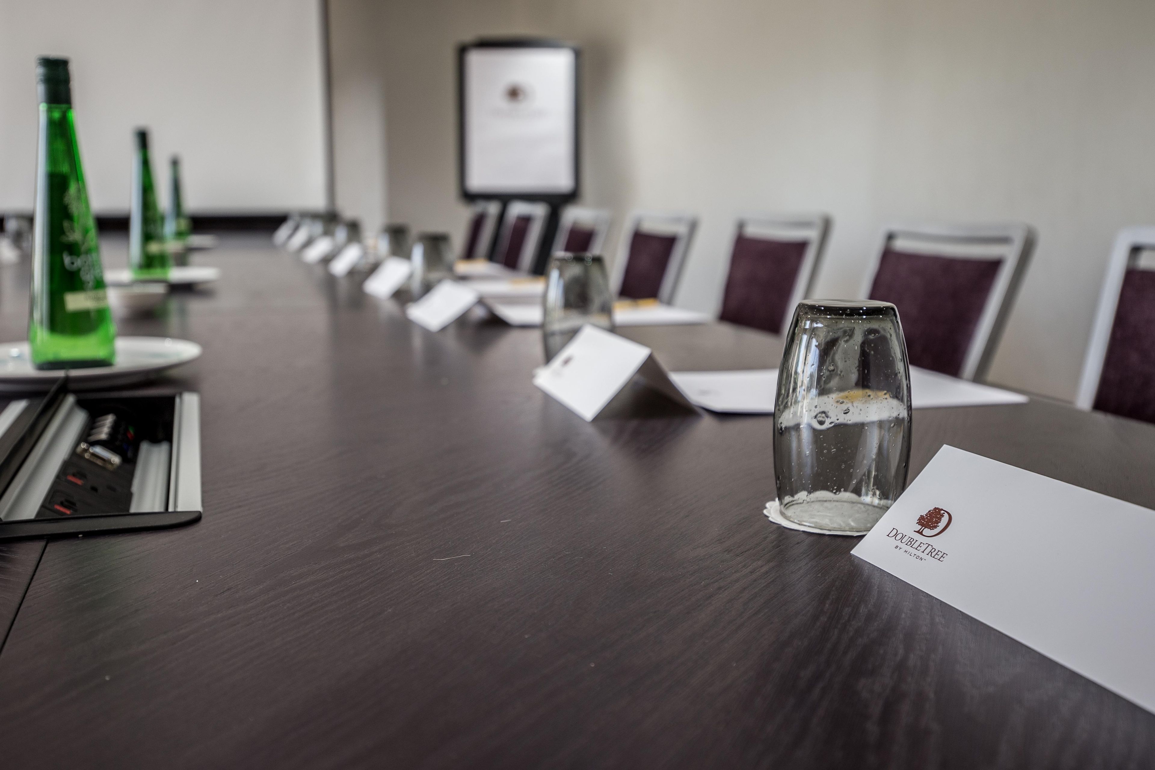 A conference table with name cards, a glass with a beverage, and green bottles in a meeting room.