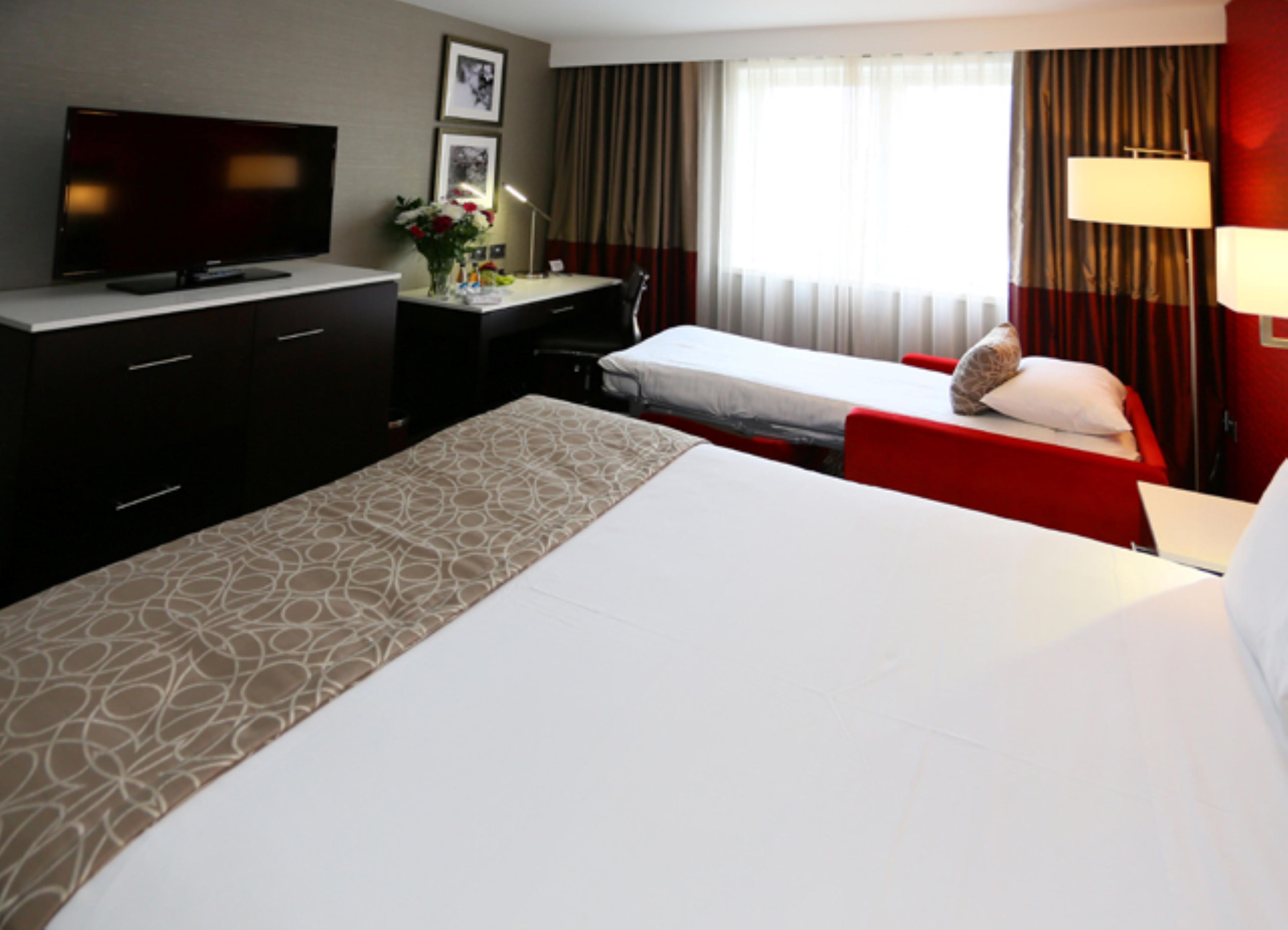 A hotel room with a bed, a desk, a television, and a window with curtains.