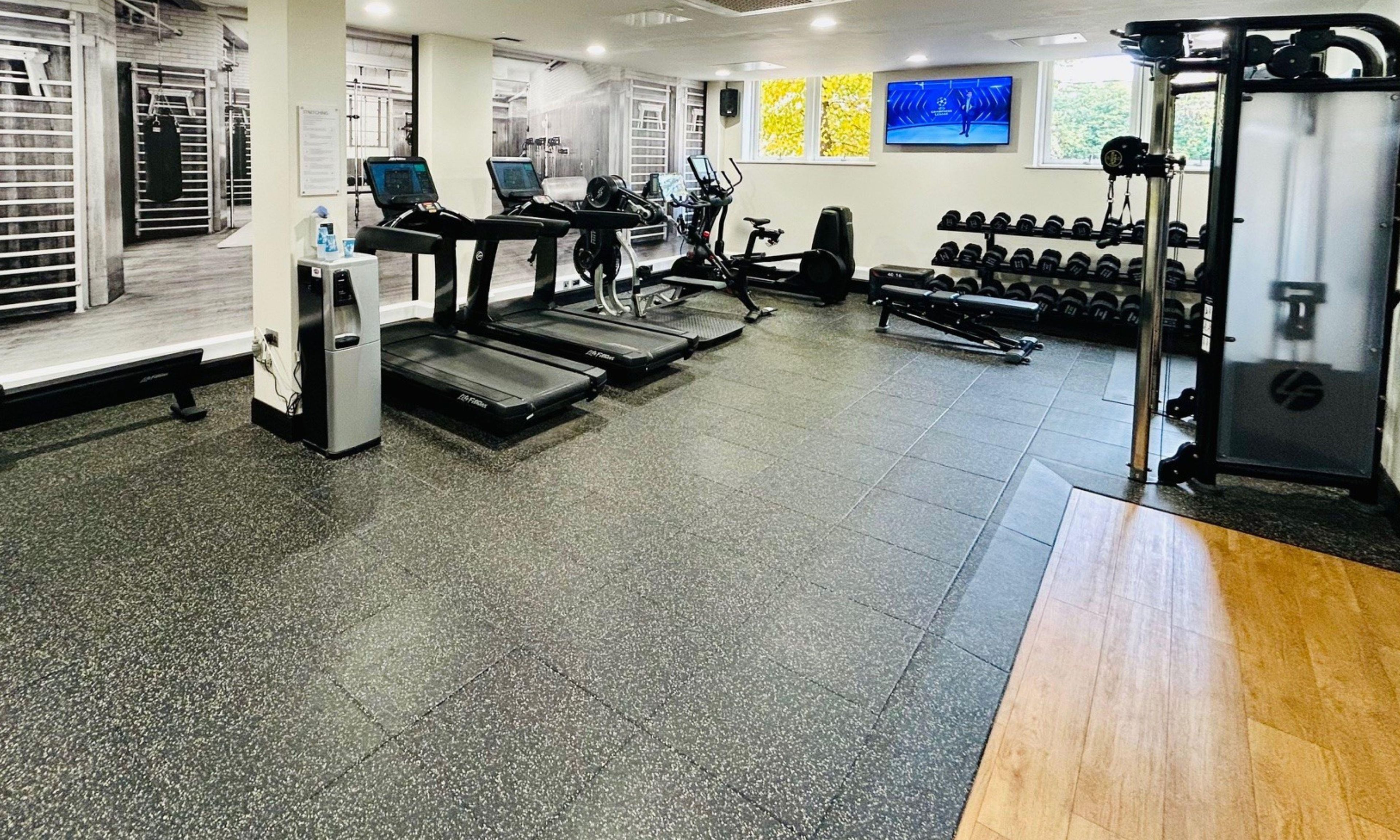 Un gimnasio con cintas de correr, máquinas de pesas y una pantalla de televisión mostrando un evento deportivo.