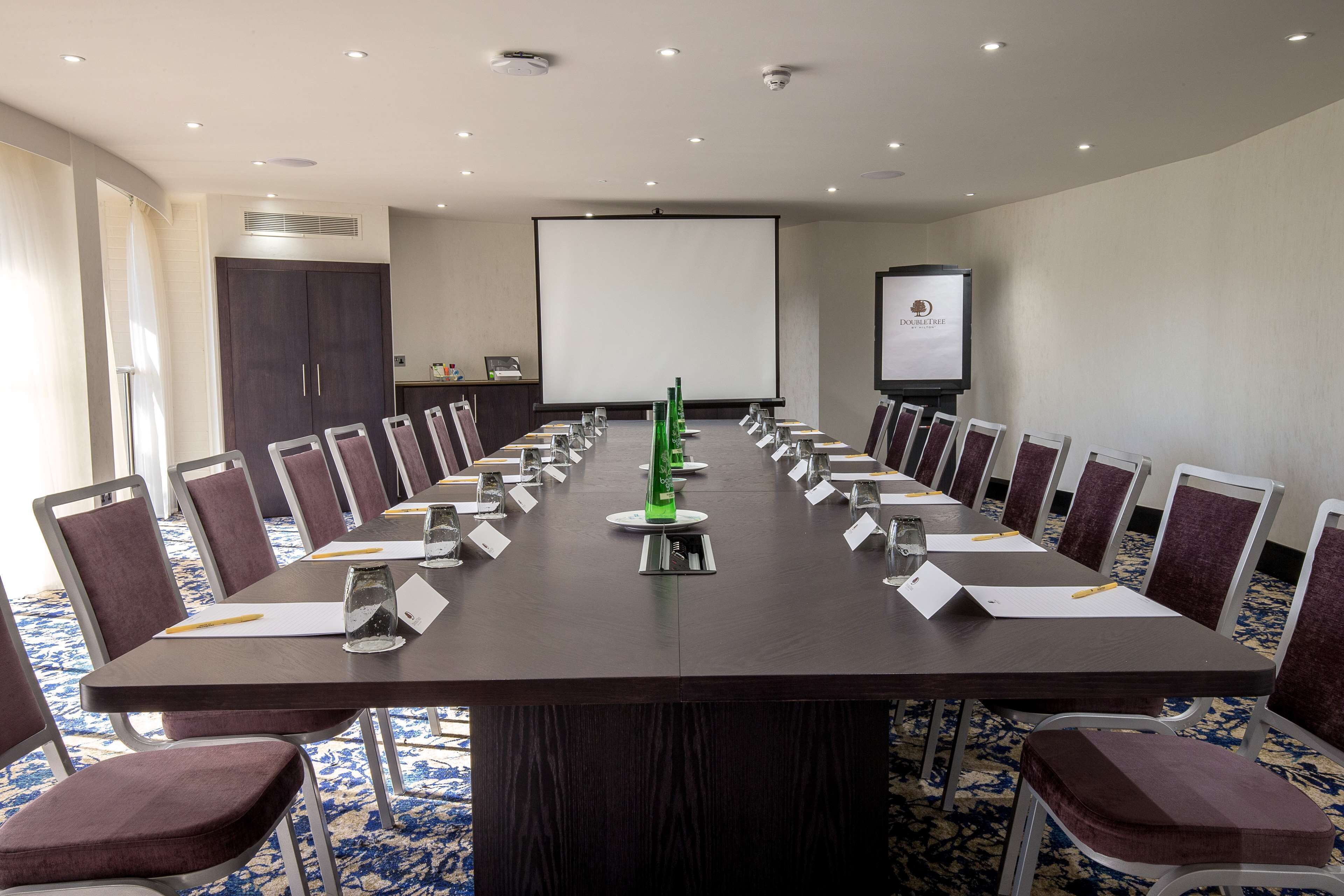 A conference room with a long table, chairs, a projector screen, and a presentation screen.