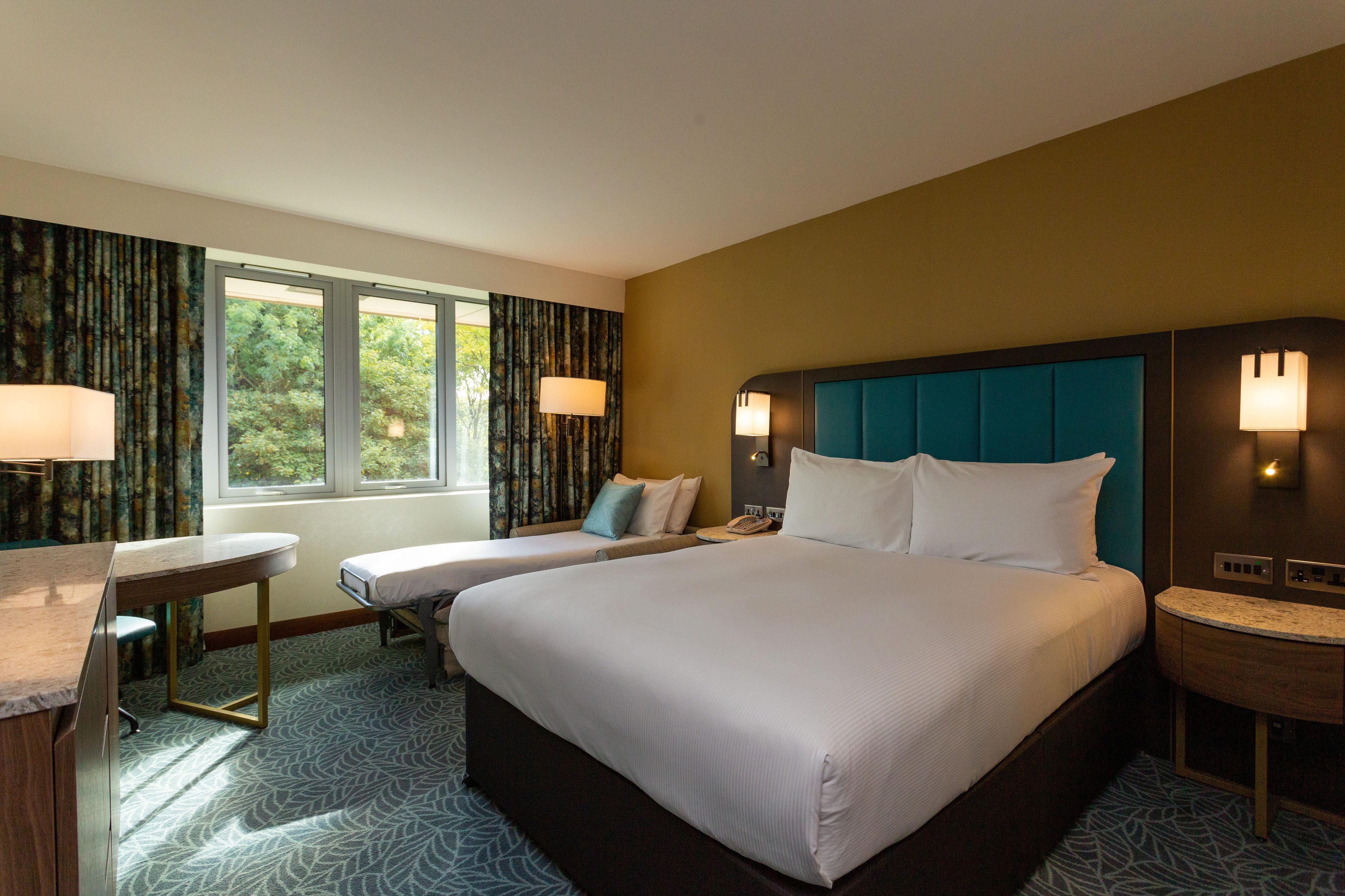 Een hotelkamer met een groot bed, twee nachtkastjes, een bureau en een raam met gordijnen.