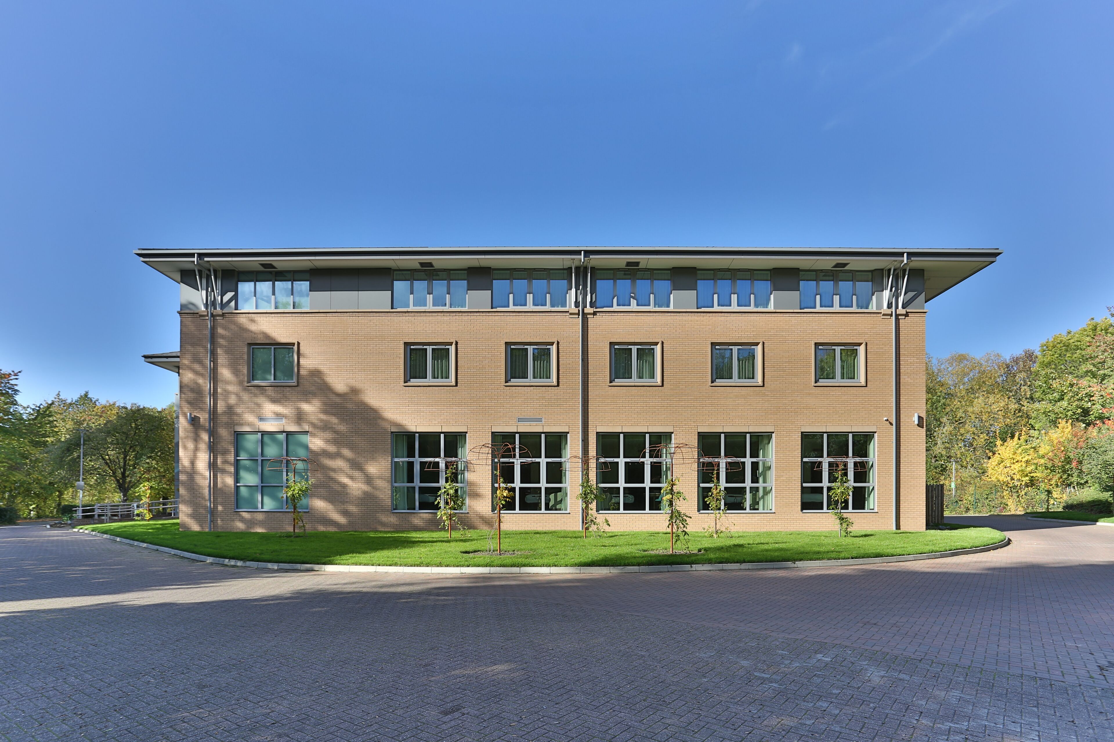 A modern two-story building with a flat roof, large windows, and a paved driveway.
