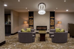 Una habitación de hotel con dos sillones grises, una mesita, un candelabro y una chimenea.