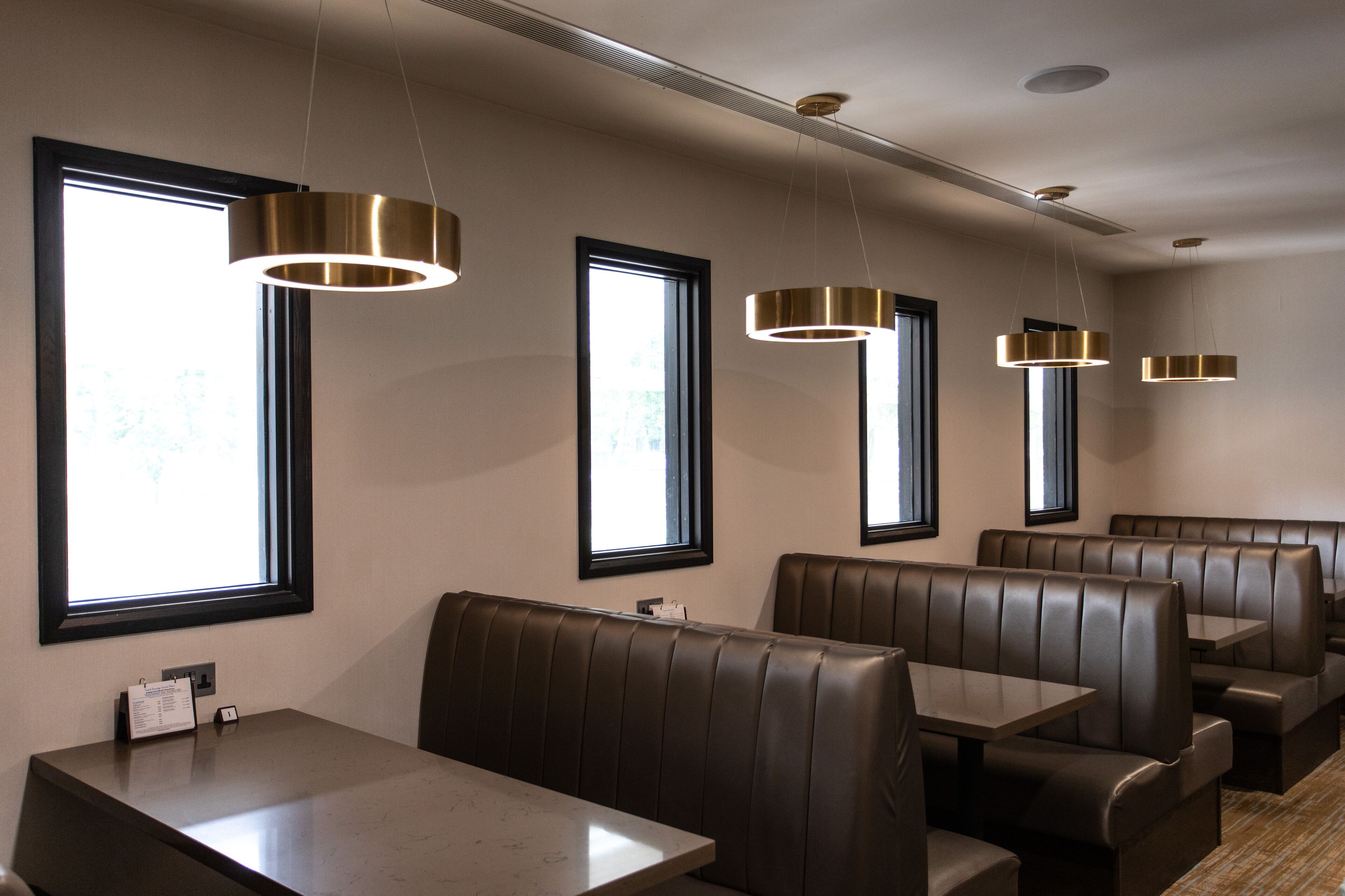 A restaurant interior with booth seating, pendant lighting, and large windows.