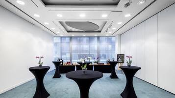 A modern conference room with round tables, a large window, and a ceiling with recessed lighting.