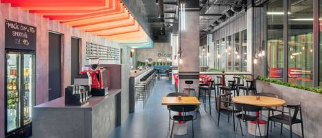 Una cafetería moderna con una barra larga, varias zonas de estar y un cartel de menú visible.