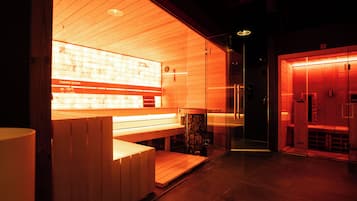 Uma sauna com bancos de madeira e divisória de vidro, painel de controle de temperatura visível e parede iluminada em vermelho.
